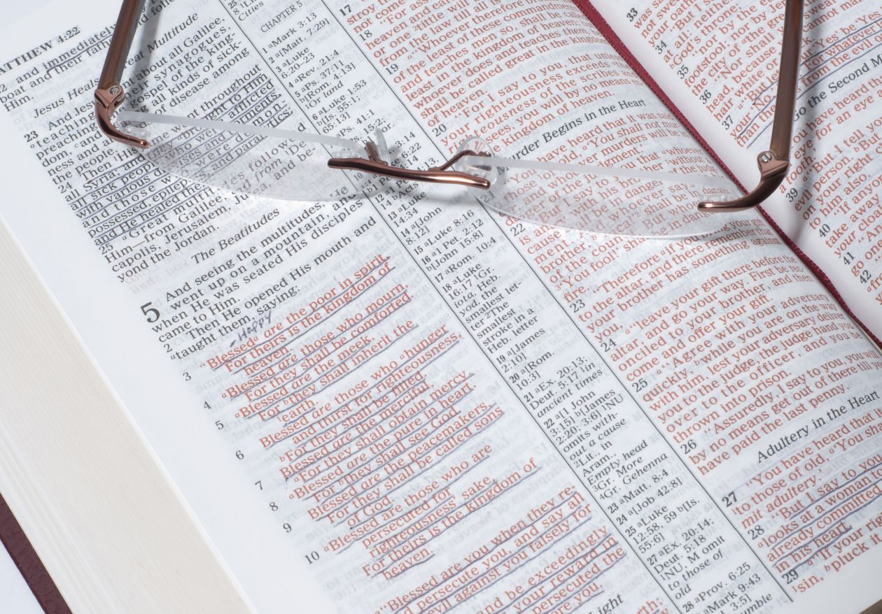 An open Bible with passages highlighted in red and a pair of reading glasses resting on the pages—perfect inspiration for a web designer seeking creativity. The clearly visible text stands out against the crisp white background.