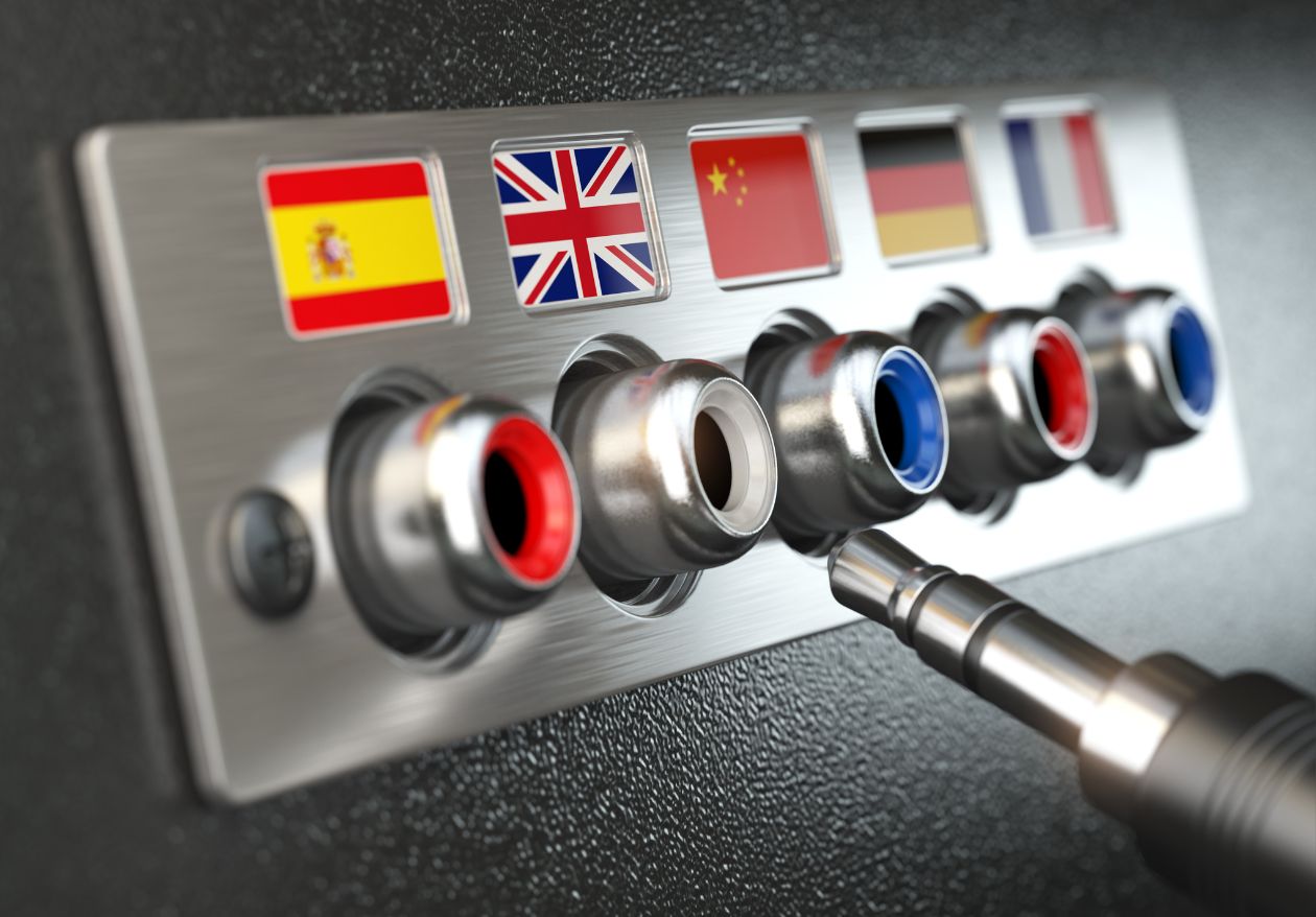 A panel with six audio jacks, each labeled with a different country’s flag: Spain, UK, China, Germany, France, and one unidentified. A cable is being plugged into the UK jack—perfect inspiration for a creative web designer or custom logo design project.