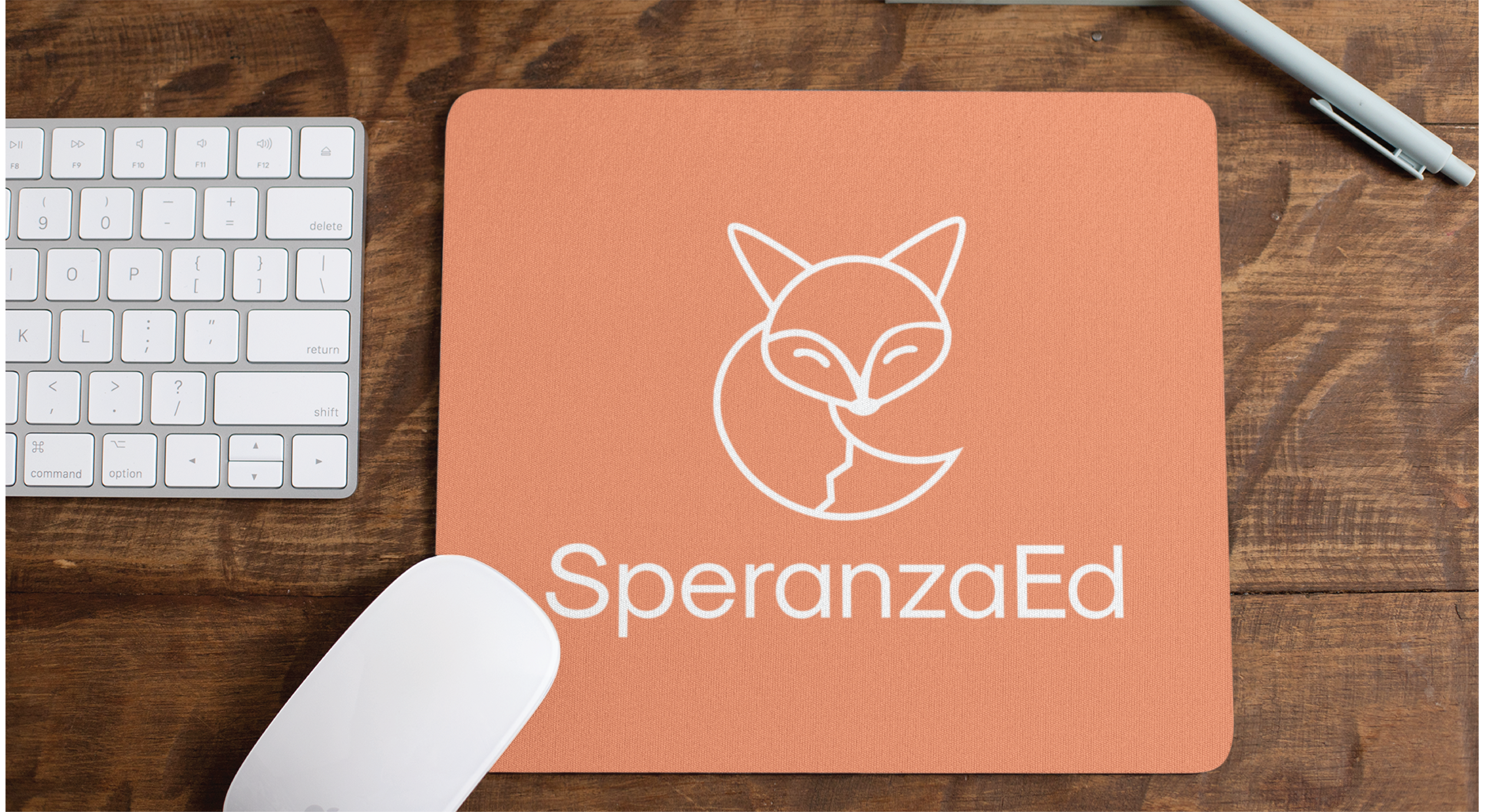 A peach-colored mouse pad featuring a white fox logo and the text SperanzaEd, known for educational consultants and branding, sits on a wooden desk beside a white keyboard, white mouse, and pen.