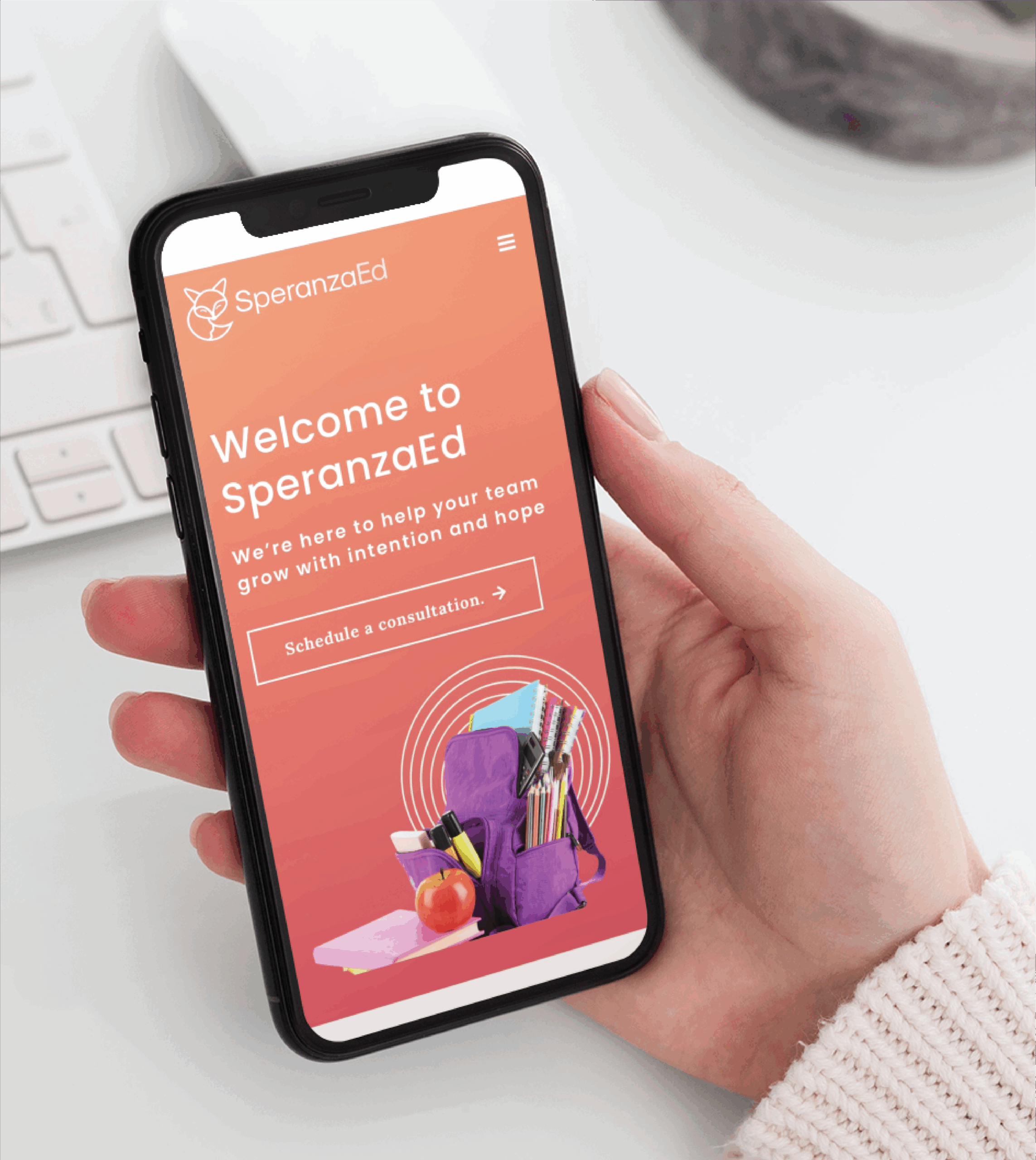 A person holds a smartphone displaying the SperanzaEd website, showcasing thoughtful website design with a welcome message, consultation button, and an image of school supplies with a purple backpack on a pink background.