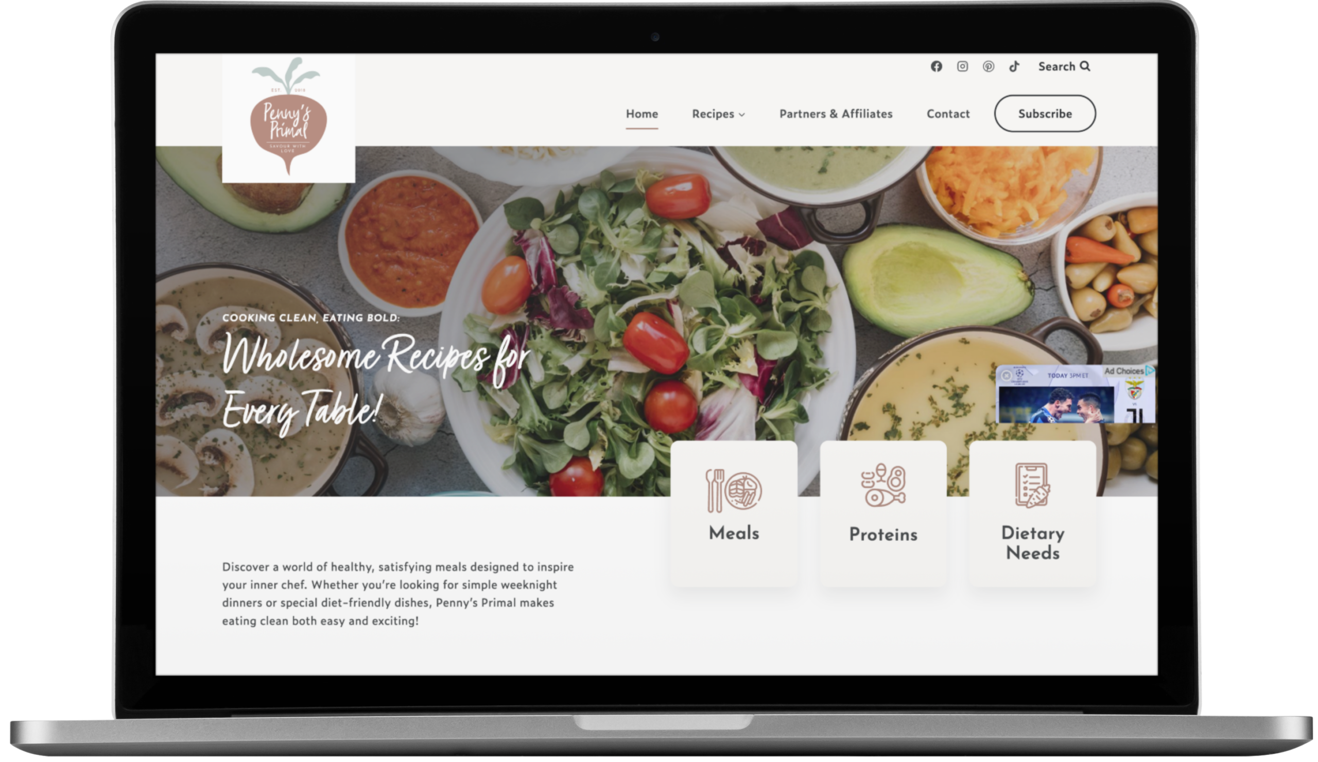 A laptop displays a food blog homepage with a salad and bowls of ingredients. The website design highlights the Pennys Primal branding, showcasing sections for recipes, meals, proteins, and dietary needs.