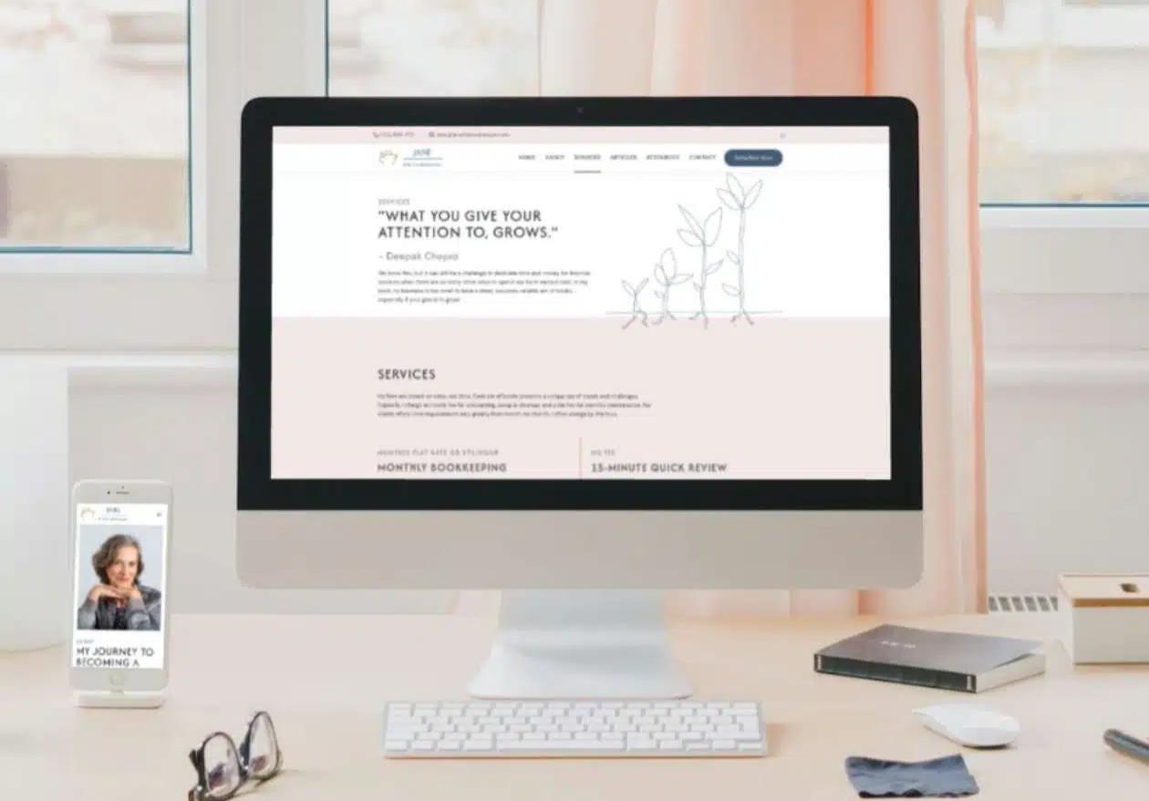 A desktop computer displays a web designer’s site with a quote and service list, while a smartphone nearby shows a woman's photo and text. The devices sit on a tidy desk with notebook, pen, wireless keyboard, and window in the background.