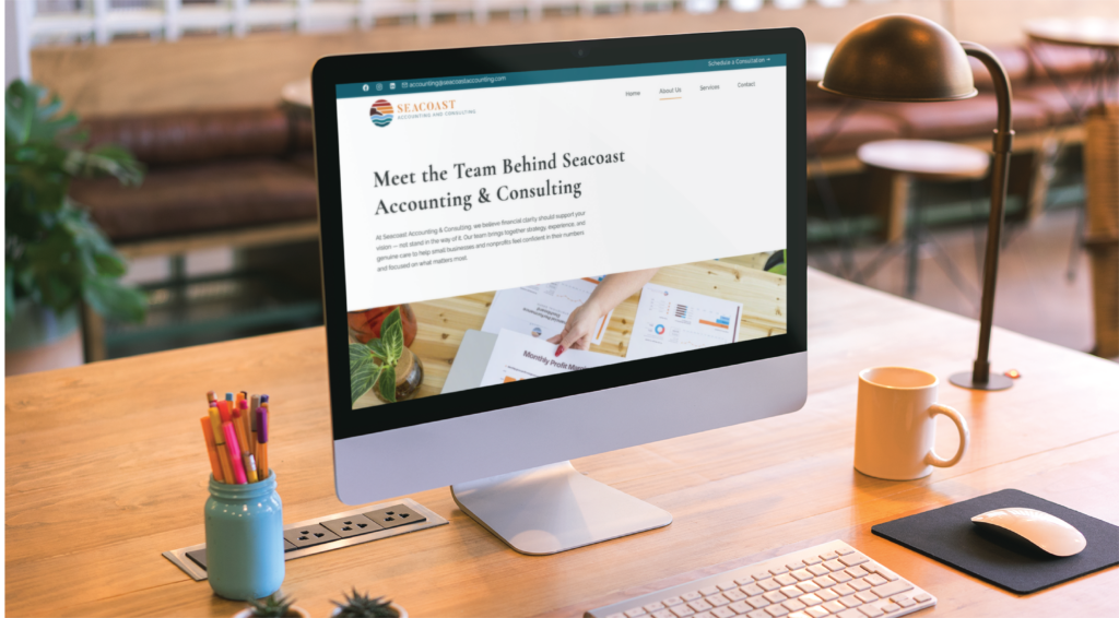 A computer screen on a wooden desk displays a website page titled Meet the Team Behind Seacoast Accounting & Consulting, showcasing their New Hampshire-based accounting support. Office supplies and a plant complete the modern workspace.