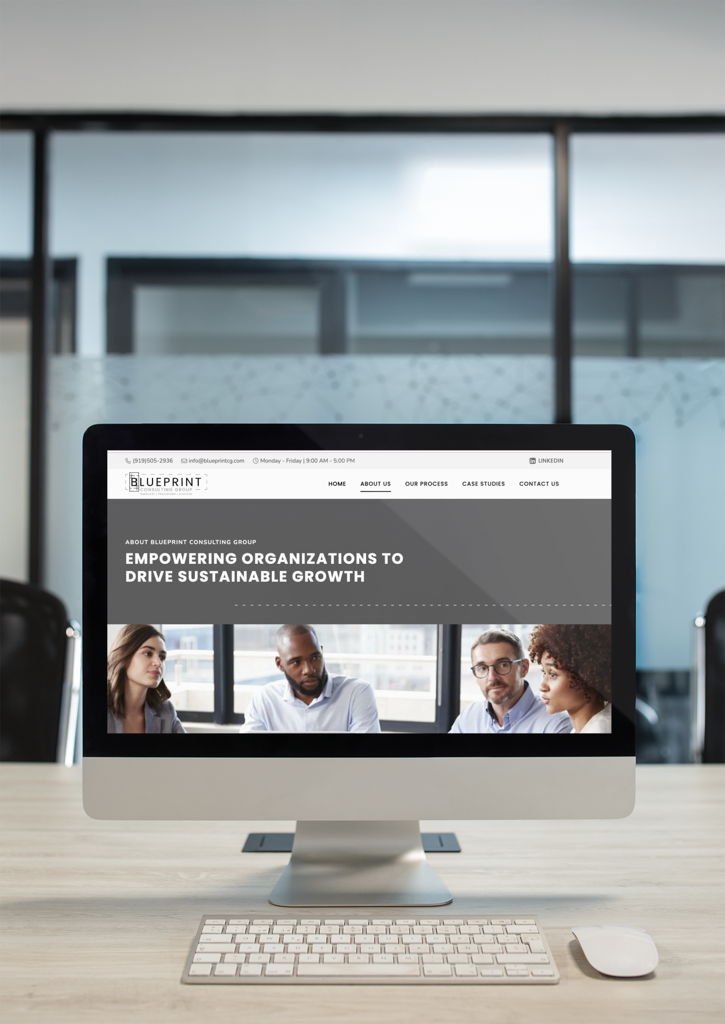 A computer screen on a desk displays a website design for a consulting firm in Raleigh NC, featuring a group of four professionals in discussion and the text Empowering organizations to drive sustainable growth.