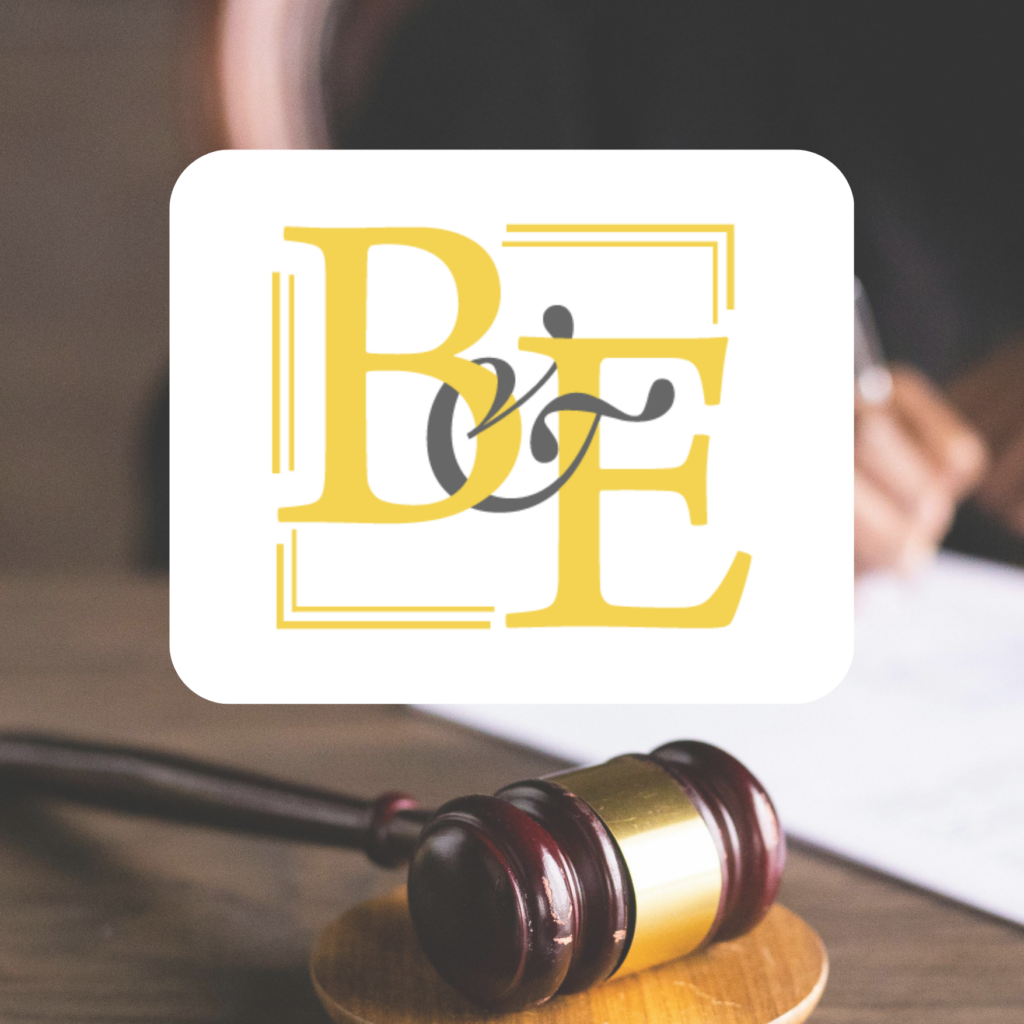 A judge’s gavel rests on a desk in the foreground. In the center, a white rectangle displays the stylized yellow letters “B & E,” showcasing standout logo design. A blurred person writes in the background.