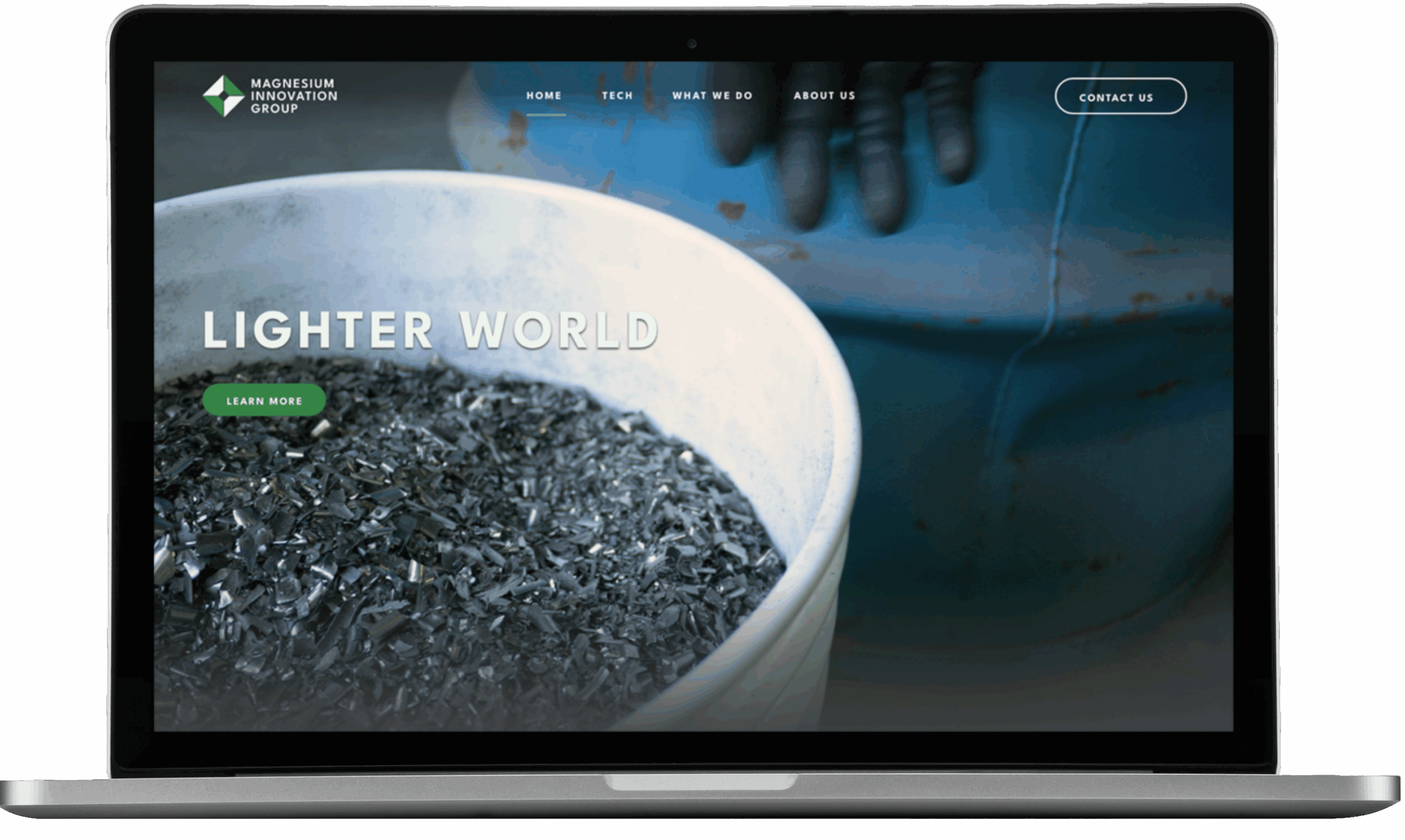 A laptop screen displays a website design for the Magnesium Innovation Group, featuring a large container of metallic shavings, the text Lighter World, navigation links, a Learn More button, and a sleek logo design.