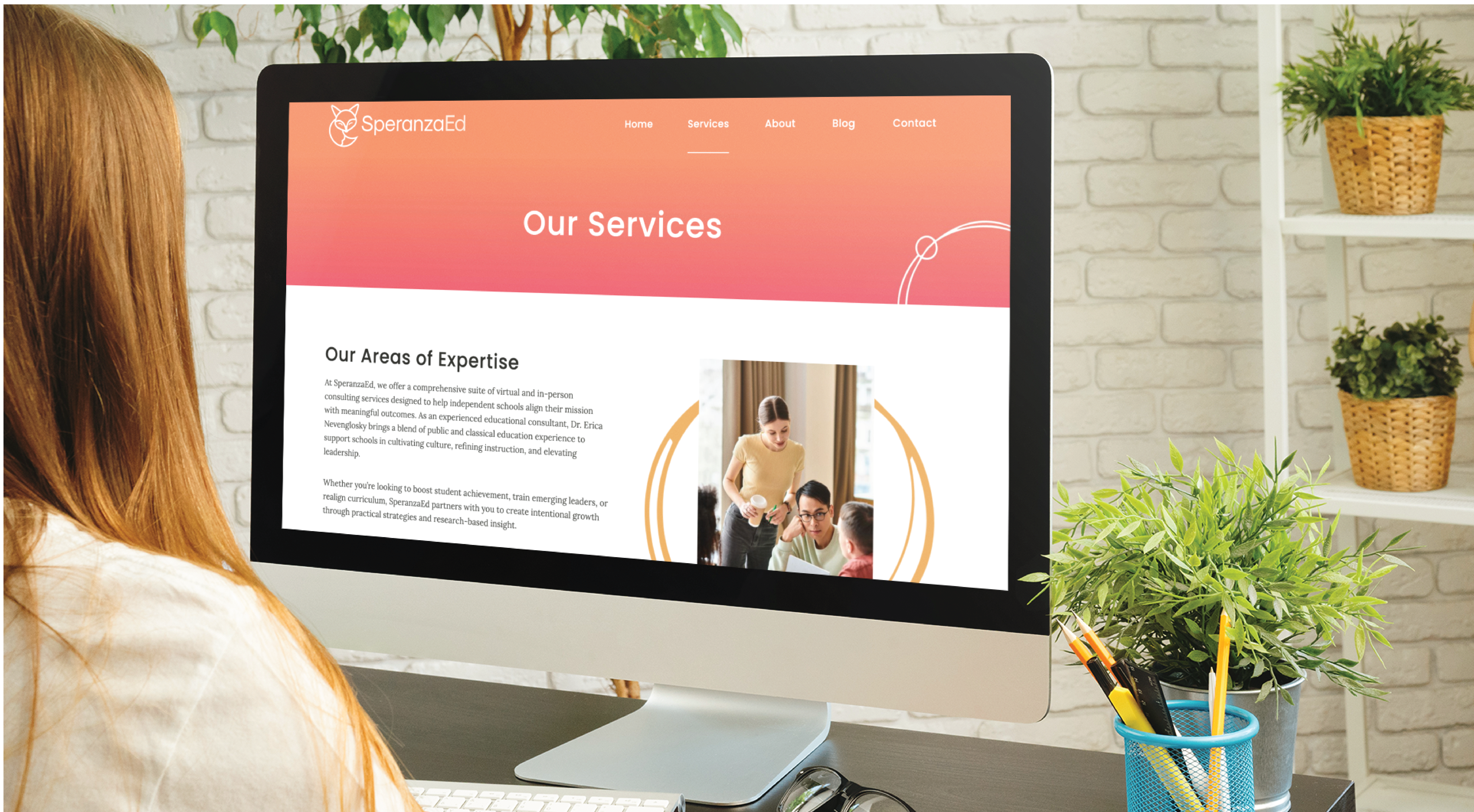 A woman with long hair sits at a desk, viewing the Our Services page of the SperanzaEd website on a desktop computer. The workspace includes a mug, pen holder, notebooks, potted plants, and hints of expert Website Design by Educational Consultants.