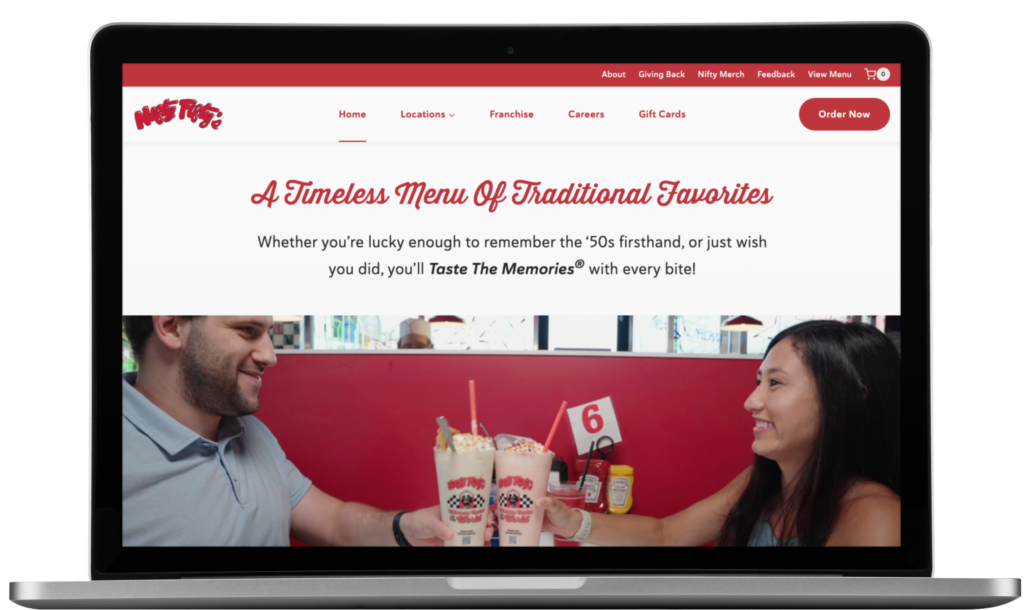 A man and woman sit at a restaurant booth in Philadelphia, smiling and clinking milkshake glasses over burgers and fries. On their laptop, the Nifty Fifty’s restaurant website design shines on screen.