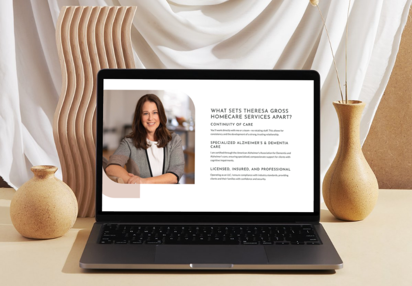 What to include in your website bio. A laptop on a beige table displays a website bio with a smiling woman’s photo and text about homecare services. Decorative vases and a sculptural piece sit beside the laptop, with draped white fabric in the background.