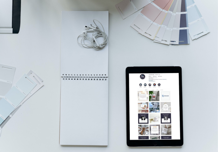 A tablet displaying a social media feed sits on a white desk next to a spiral notebook, earphones, and scattered color swatches, evoking a workspace where the hidden language of design shapes effective brand messaging.