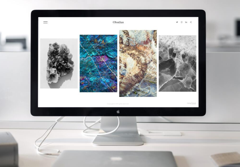 A desktop computer displays a website titled “Obsidian,” featuring four images of colorful rock and mineral textures in a minimalist interface—a striking example of how the hidden language of design shapes brand messaging. The computer sits on a clean, modern desk.