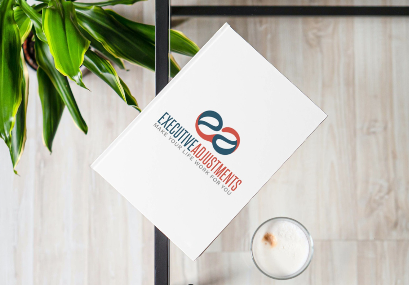 A white book titled Executive Adjustments with a stylized logo—reflecting the hidden language of design—rests on a light wooden table beside a green plant and a glass of milk.