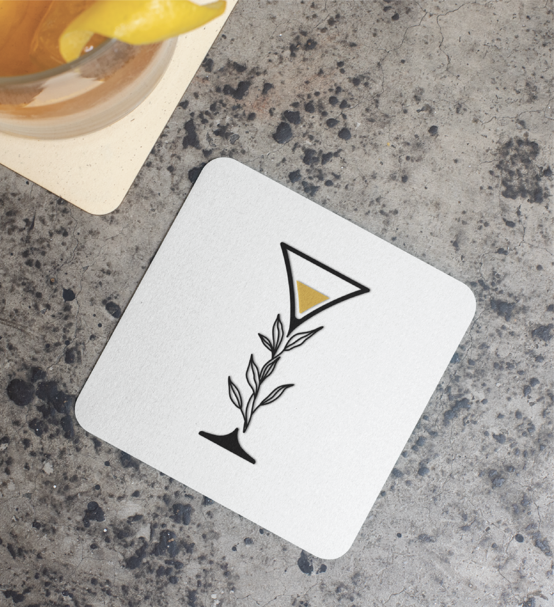 A white square coaster with a minimalist black martini glass and leafy stem design, featuring a small yellow triangle, showcases Custom Logo Design perfect for a Restaurant in Florida. It sits on a speckled gray surface next to a drink with a lemon twist.