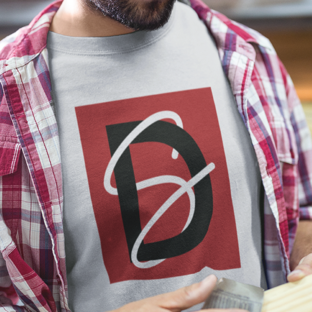 A person wearing a plaid shirt over a t-shirt featuring a custom logo design with a large stylized D on a red rectangle background. The D is intersected by white curved lines. The person's face is partially out of frame.