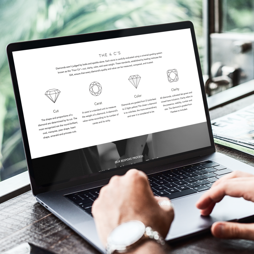 A person types on a laptop displaying a custom website design about the 4 Cs of diamonds—Cut, Carat, Color, and Clarity—with diagrams and descriptions, in front of a window showing New York’s green foliage outside.