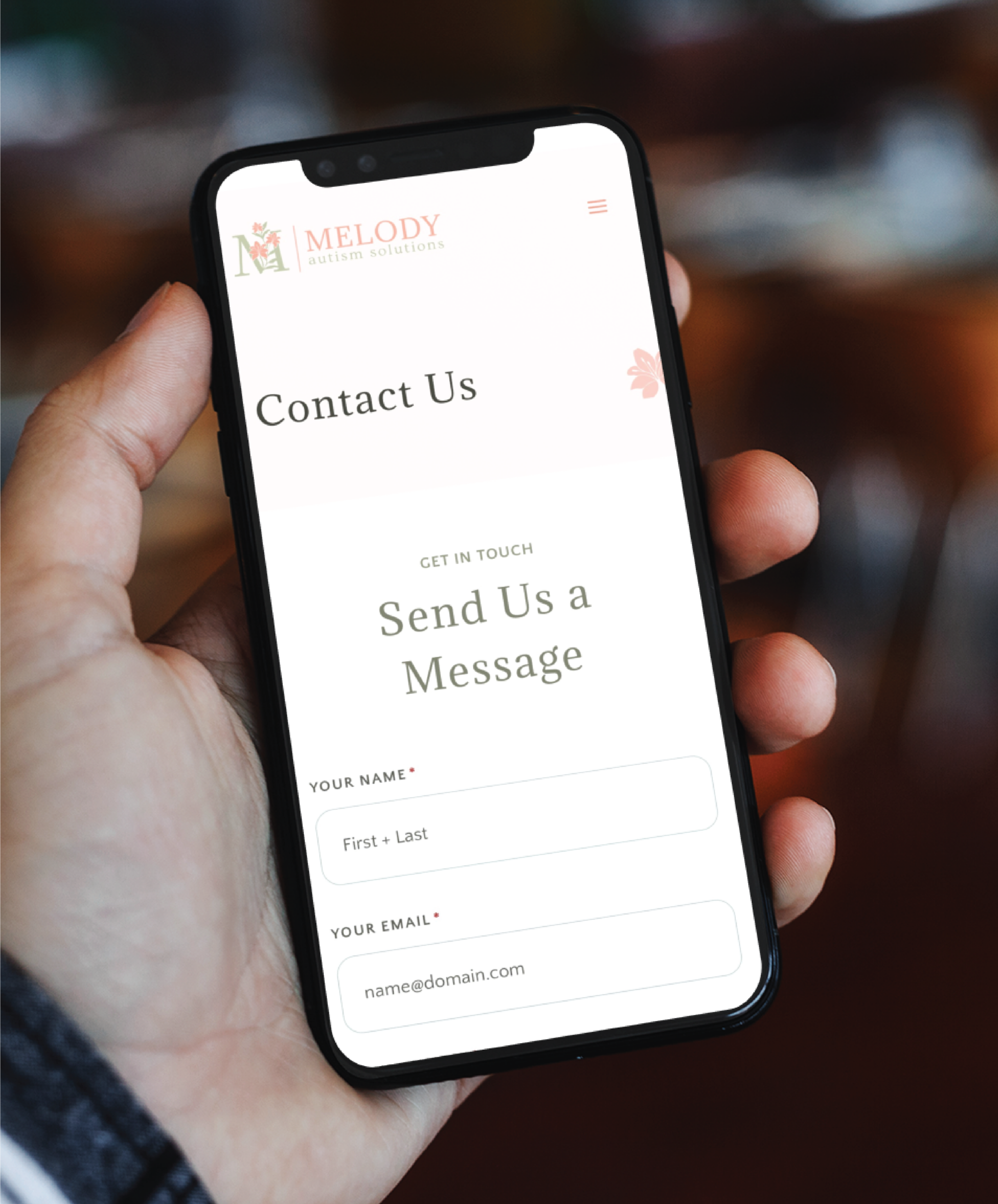 A hand holding a smartphone displays the Melody Caption Solutions Contact Us page, featuring name, email, and message fields—ideal for Philadelphia businesses seeking custom website design inspired by a 1950s-themed diner.