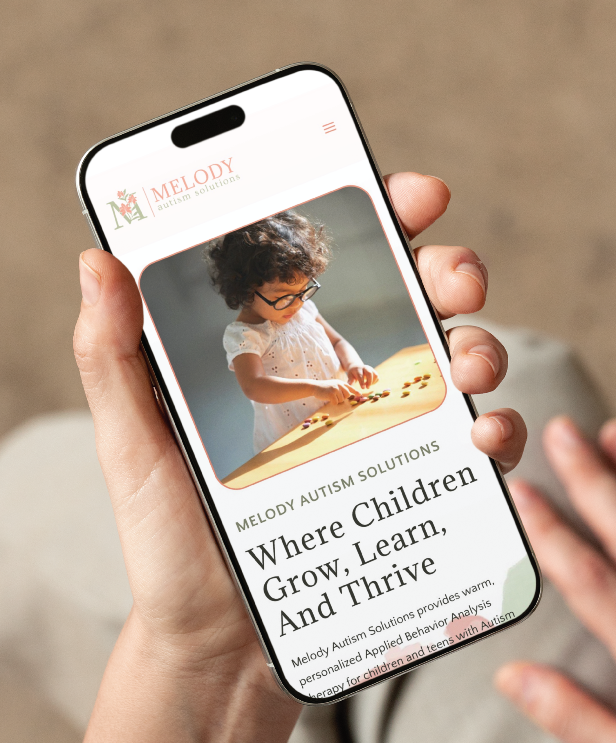 A hand holds a smartphone displaying the Melody Autism Solutions custom website design, featuring a photo of a young girl with glasses playing with toys and the headline Where Children Grow, Learn, And Thrive in Philadelphia PA.