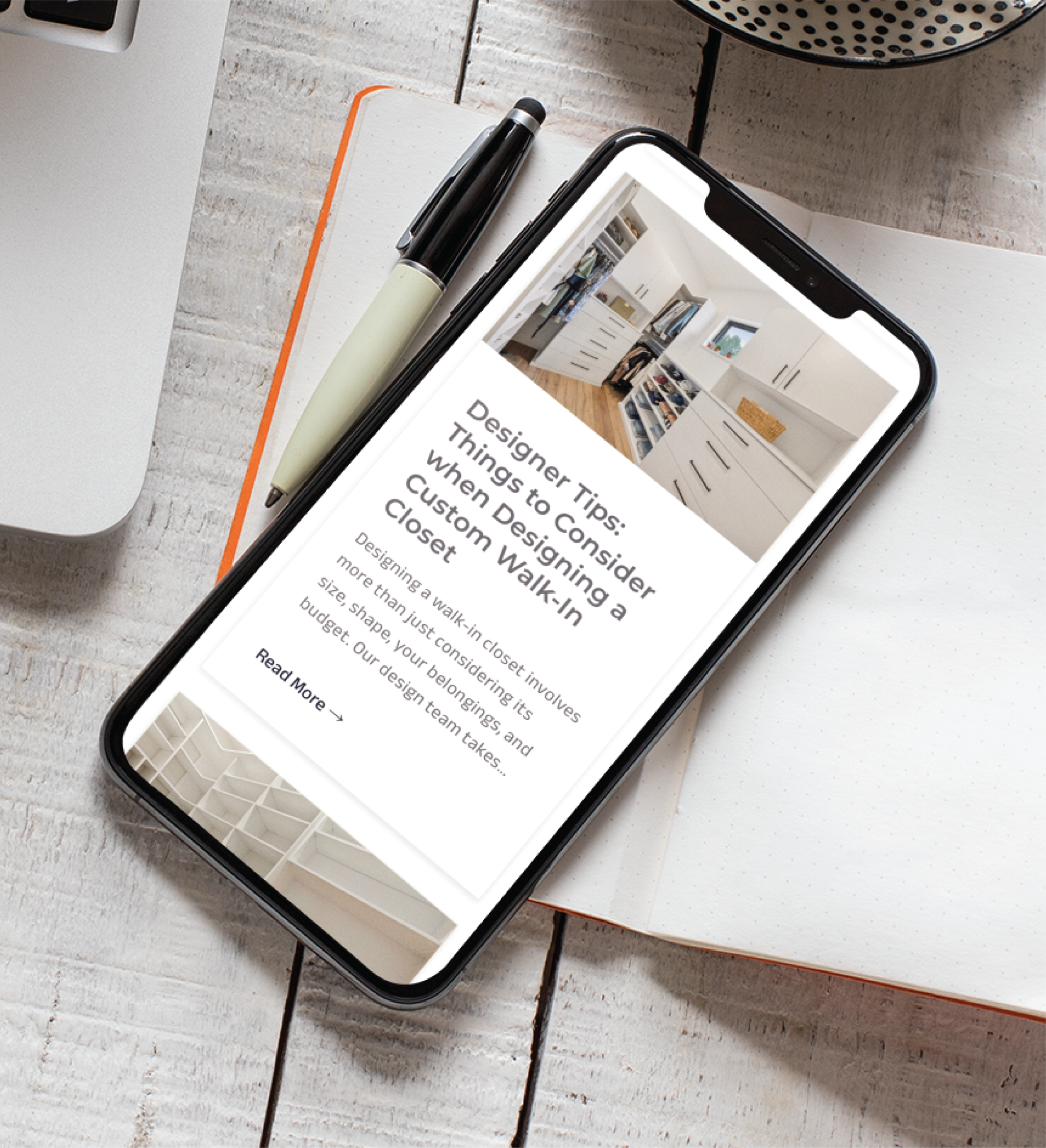 A smartphone displaying an article titled Designer Tips: Things to Consider When Designing a Custom Walk-in Closet rests on an open notebook beside a pen and a partial view of a laptop, perfect inspiration for custom web design ideas in Pennsylvania.