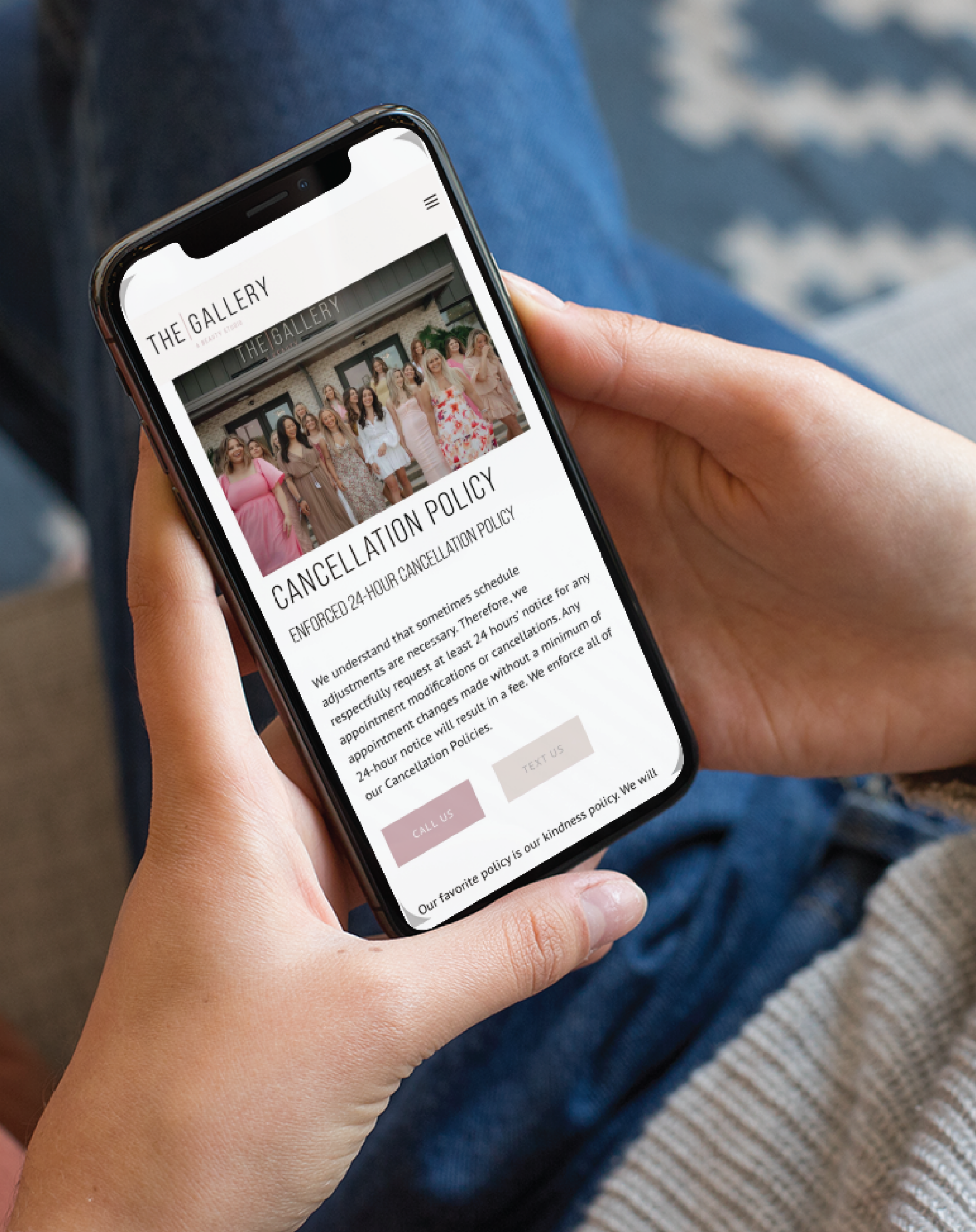 A person holding a smartphone displays The Gallery Beauty Salon’s website, showing a group photo and details on their 24-hour cancellation policy. Seated in blue jeans and a light top, they browse the sleek website design for this South Carolina salon.