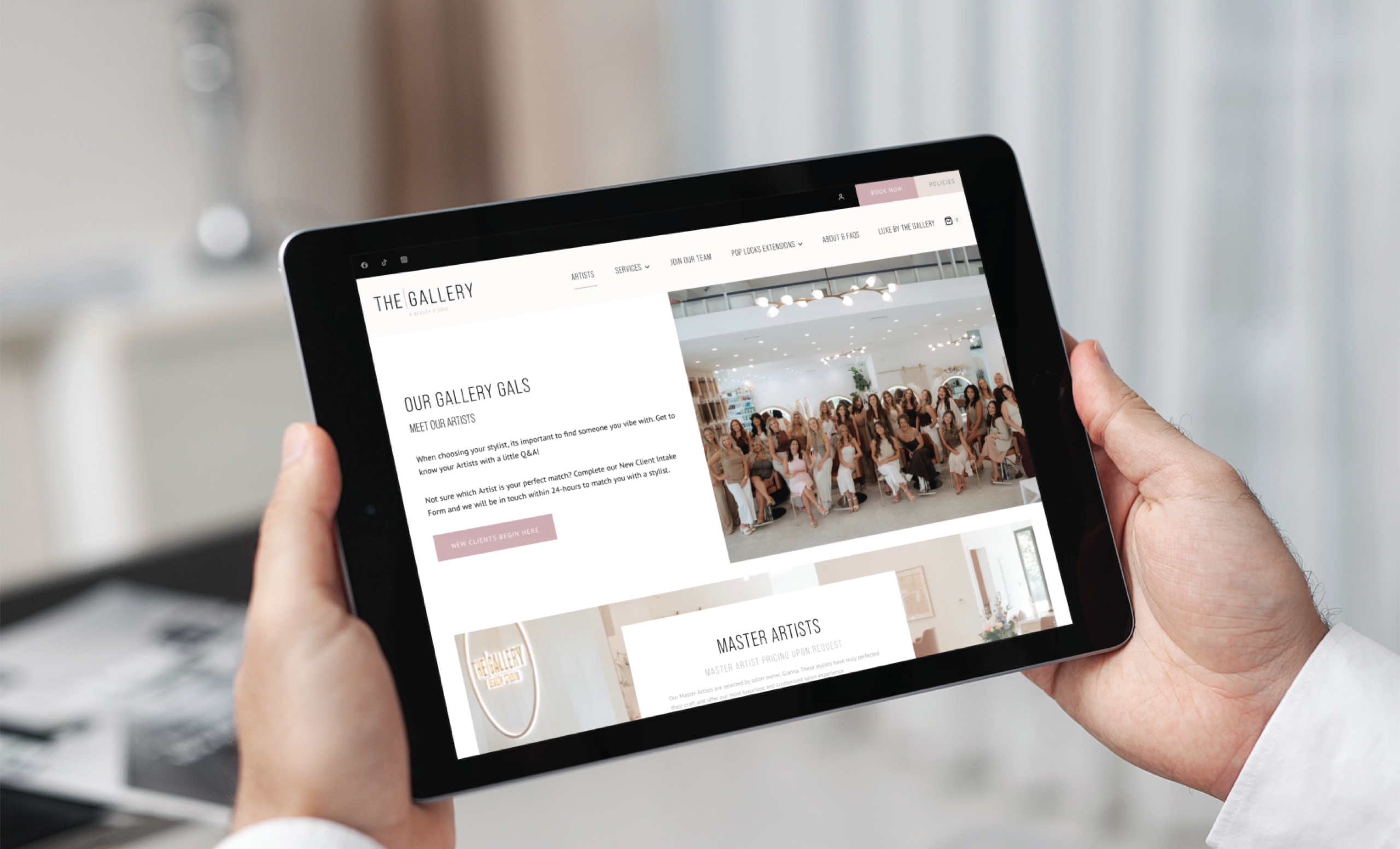 A person holds a tablet displaying a website called The Gallery, featuring modern website design with a group photo of women in a bright room and sections highlighting artists and gallery information in South Carolina.