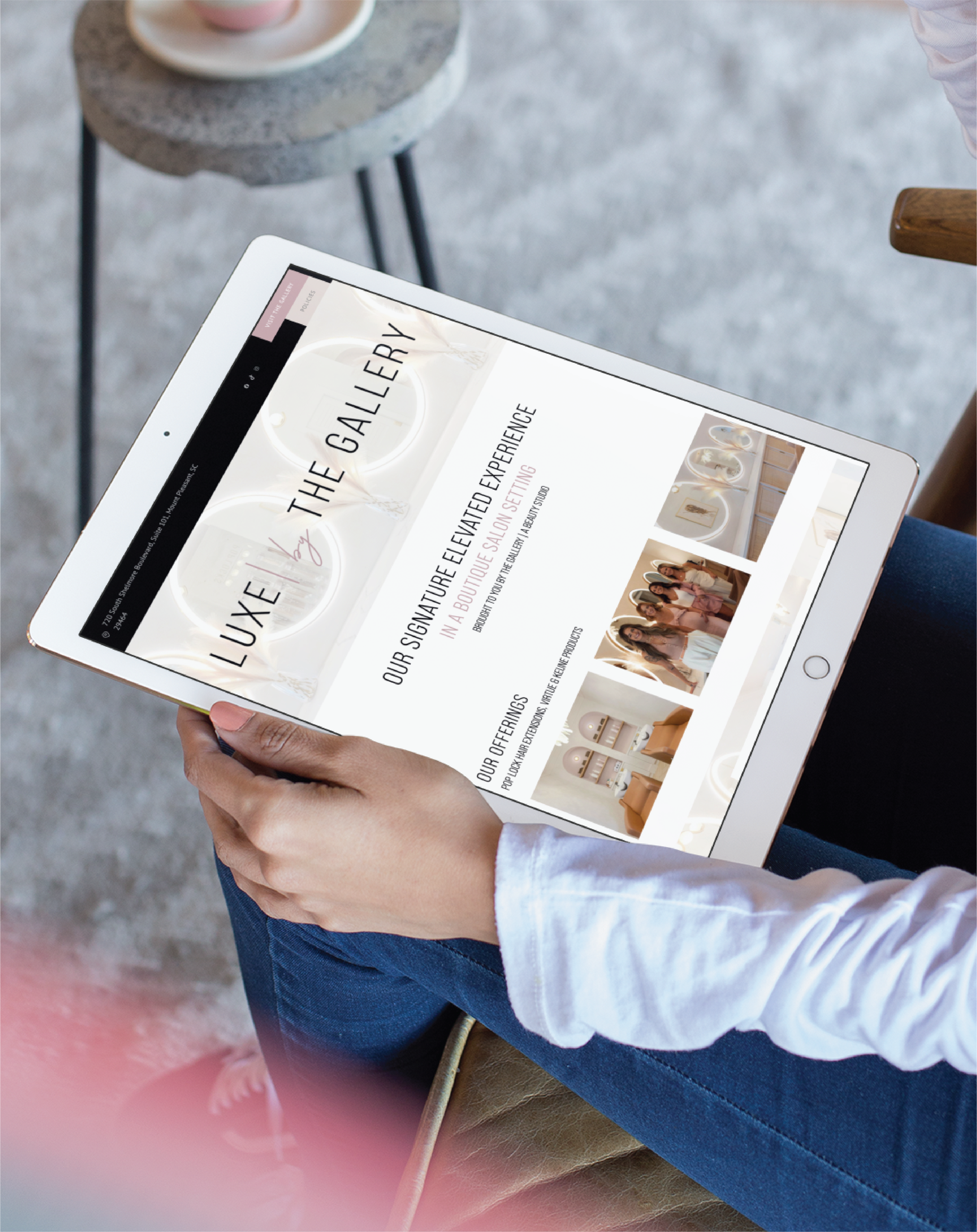 A person wearing a white long-sleeve shirt holds a tablet displaying a website called LUXE THE GALLERY, showcasing ceramics and text about a curated retail experience, highlighting elegant website design inspired by South Carolina.