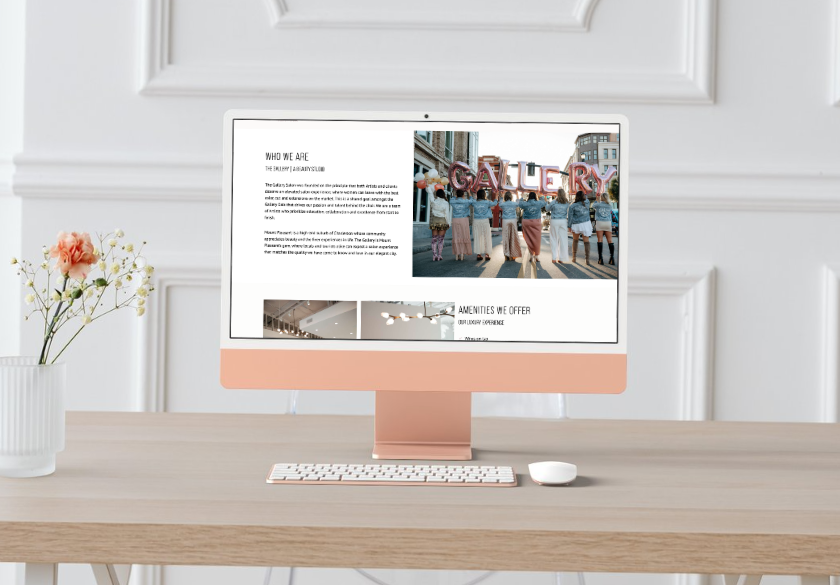 A modern desktop computer with a peach-colored keyboard and mouse displays a Hair Salon Website Design. The screen shows a group photo with large GALLERY letters and text about Who we are. A vase with flowers is on the desk.