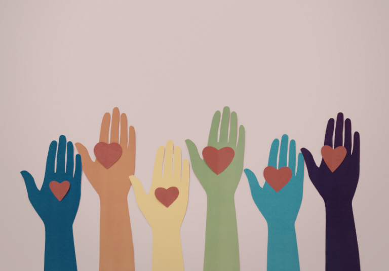 Six colorful paper cutout hands in different skin tones are raised upright, each with a red heart shape on the palm, against a light pink background.