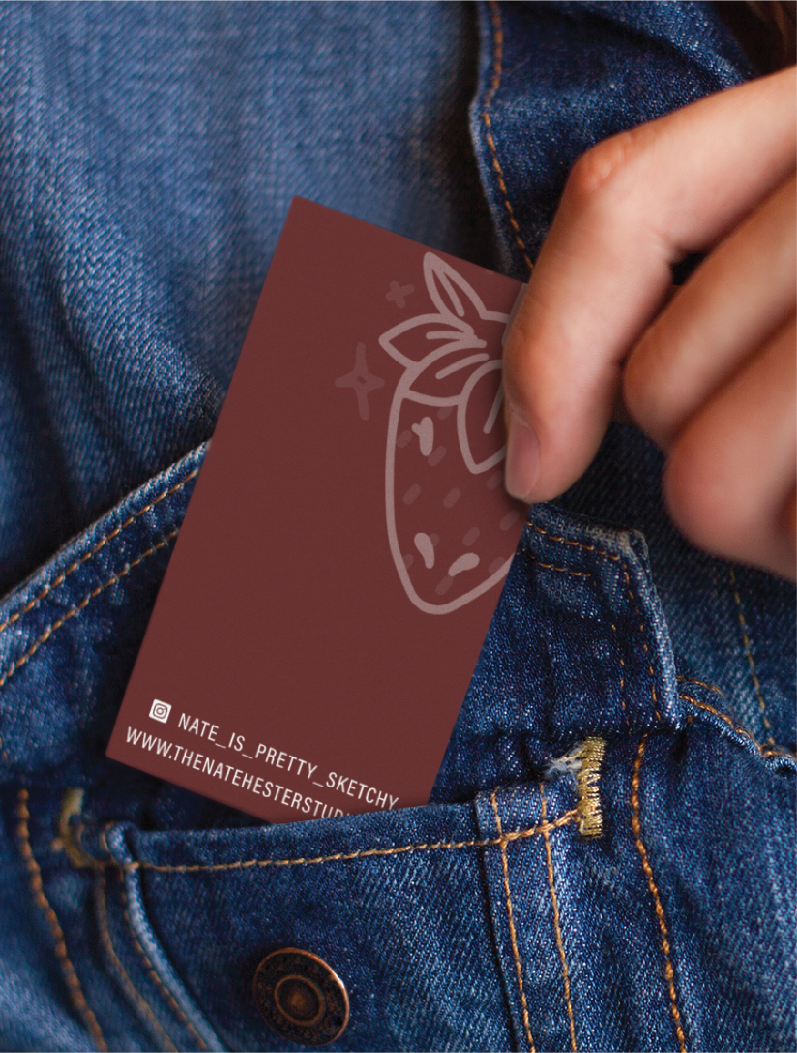 A hand slides a maroon business card with a strawberry illustration and social media info—perfect for Tennessee life coaches—into the pocket of a blue denim jacket.