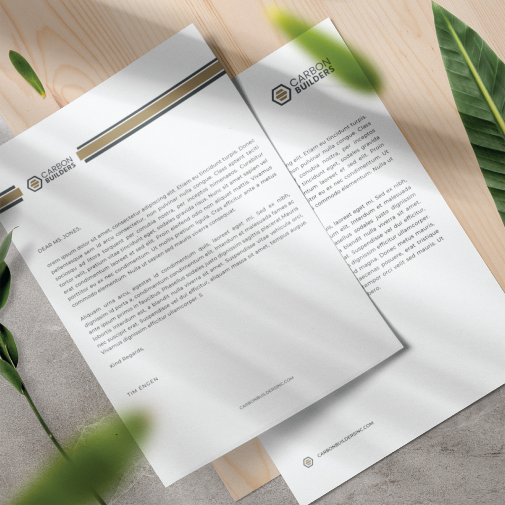 Open brochures featuring the Carbon Builders logo on white pages, laid on a light wooden surface with green leaves nearby.