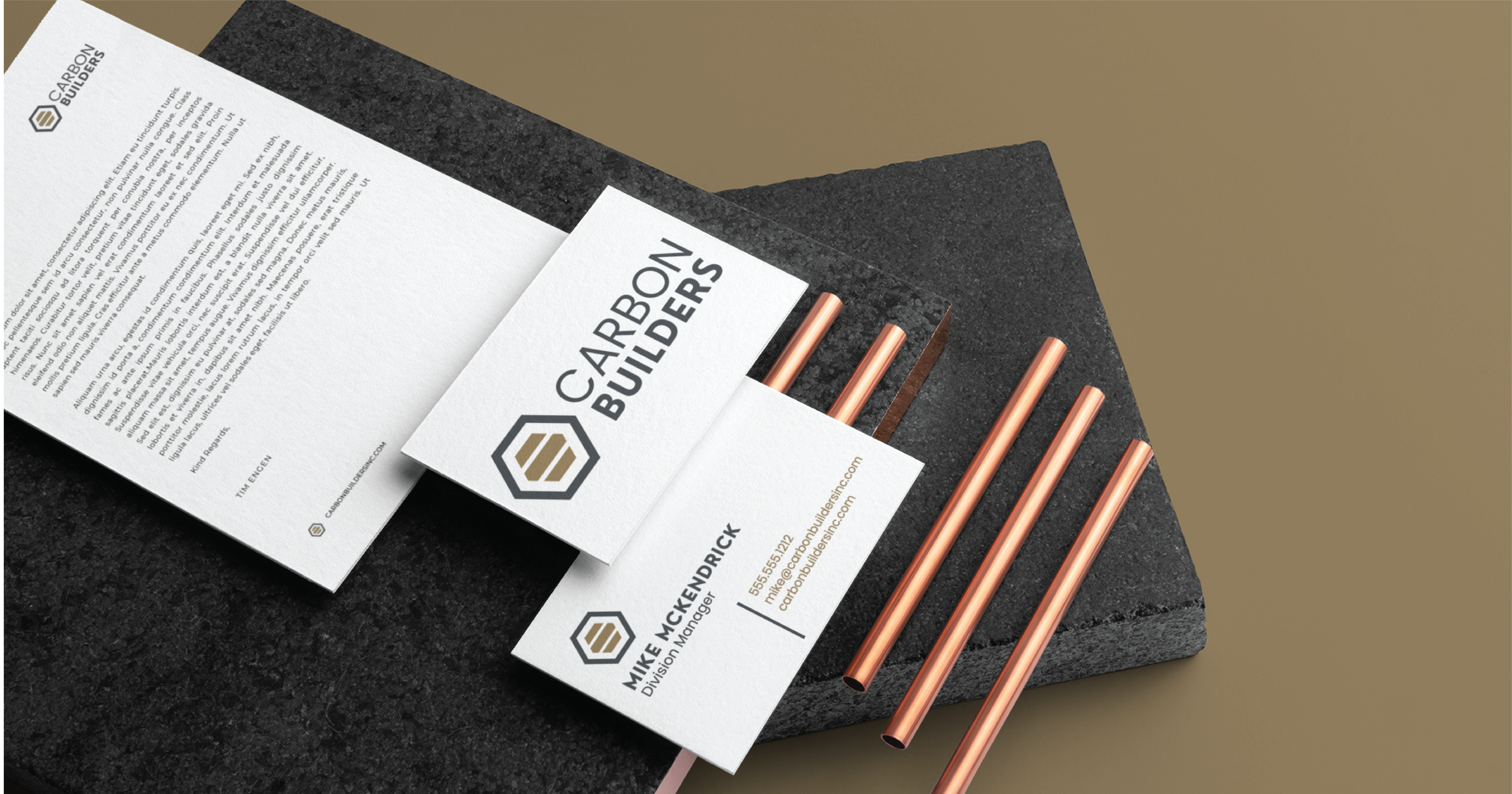 A stationery design set for Carbon Builders, a Michigan general contractor, featuring a letterhead and business cards displayed on black stone slabs with copper-colored metal rods. The modern typography and hexagonal logo complete the sleek look.