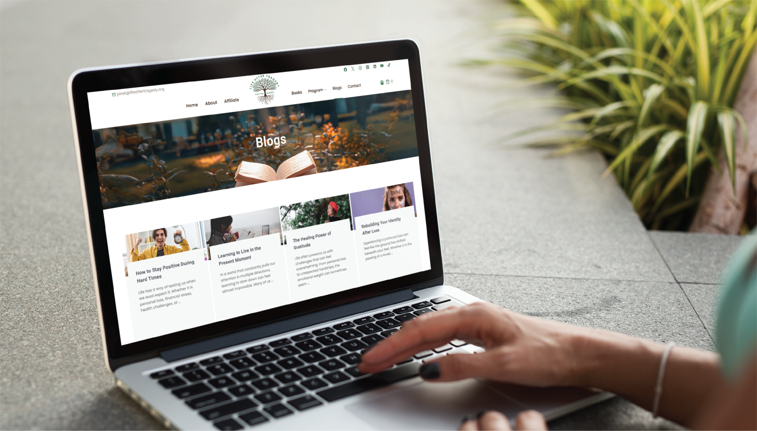 A person uses a laptop outdoors in Pennsylvania, browsing a website with a Blogs section featuring articles and images about counseling services. Green plants create a peaceful background.