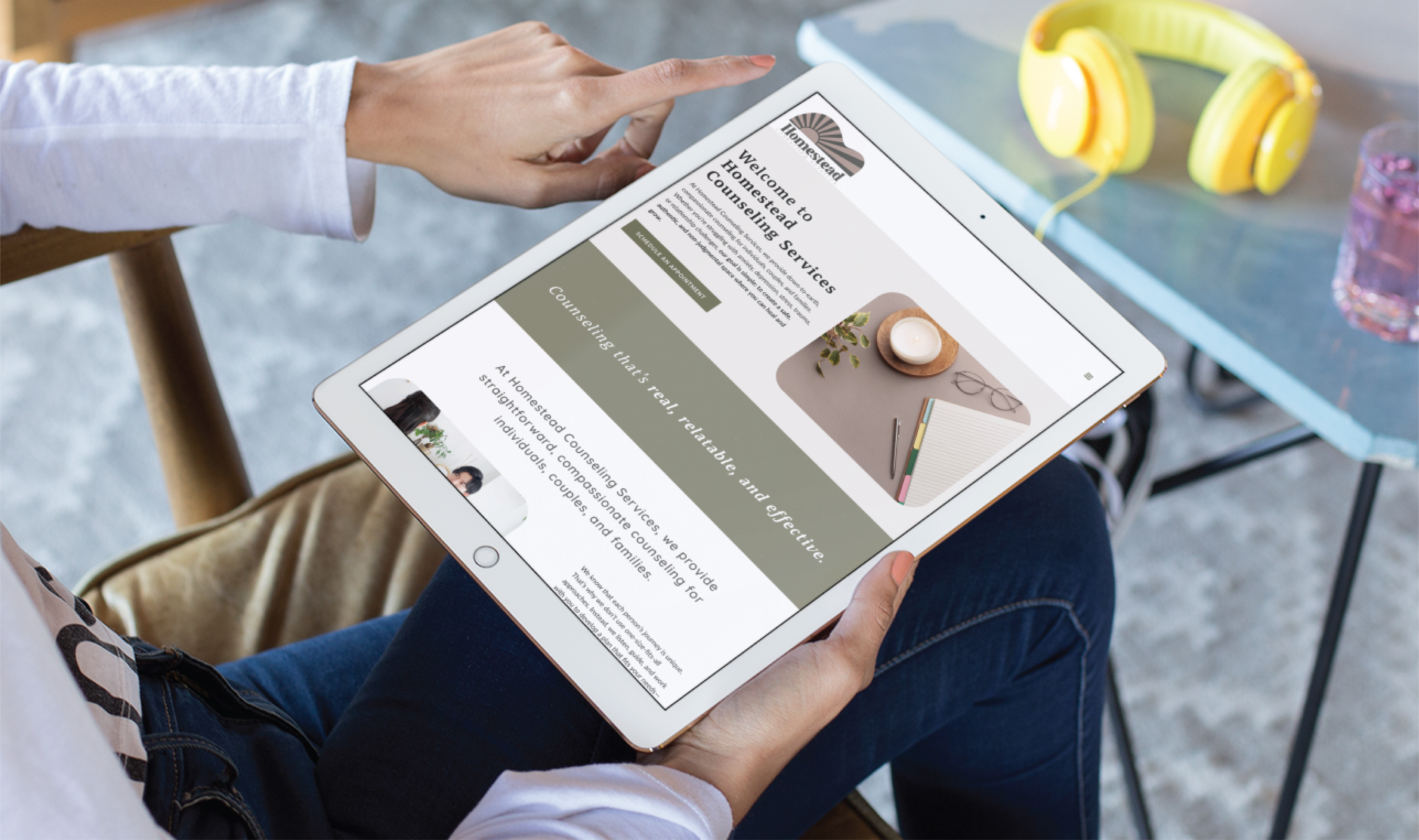 A person sits and holds a tablet, browsing a Pennsylvania counseling service website with information, images of a notebook and coffee, and a green banner; yellow headphones rest on a nearby table.