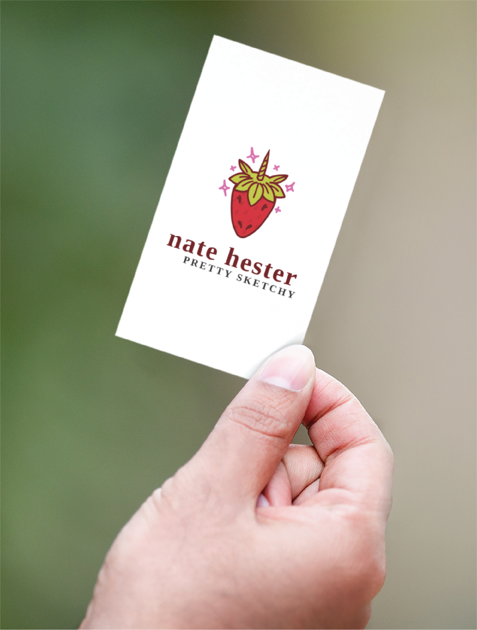 A hand holding a business card featuring an illustrated strawberry with sparkles above the name “nate hester,” Life Coach, and the tagline “PRETTY SKETCHY”—set against a blurred green background in Tennessee.