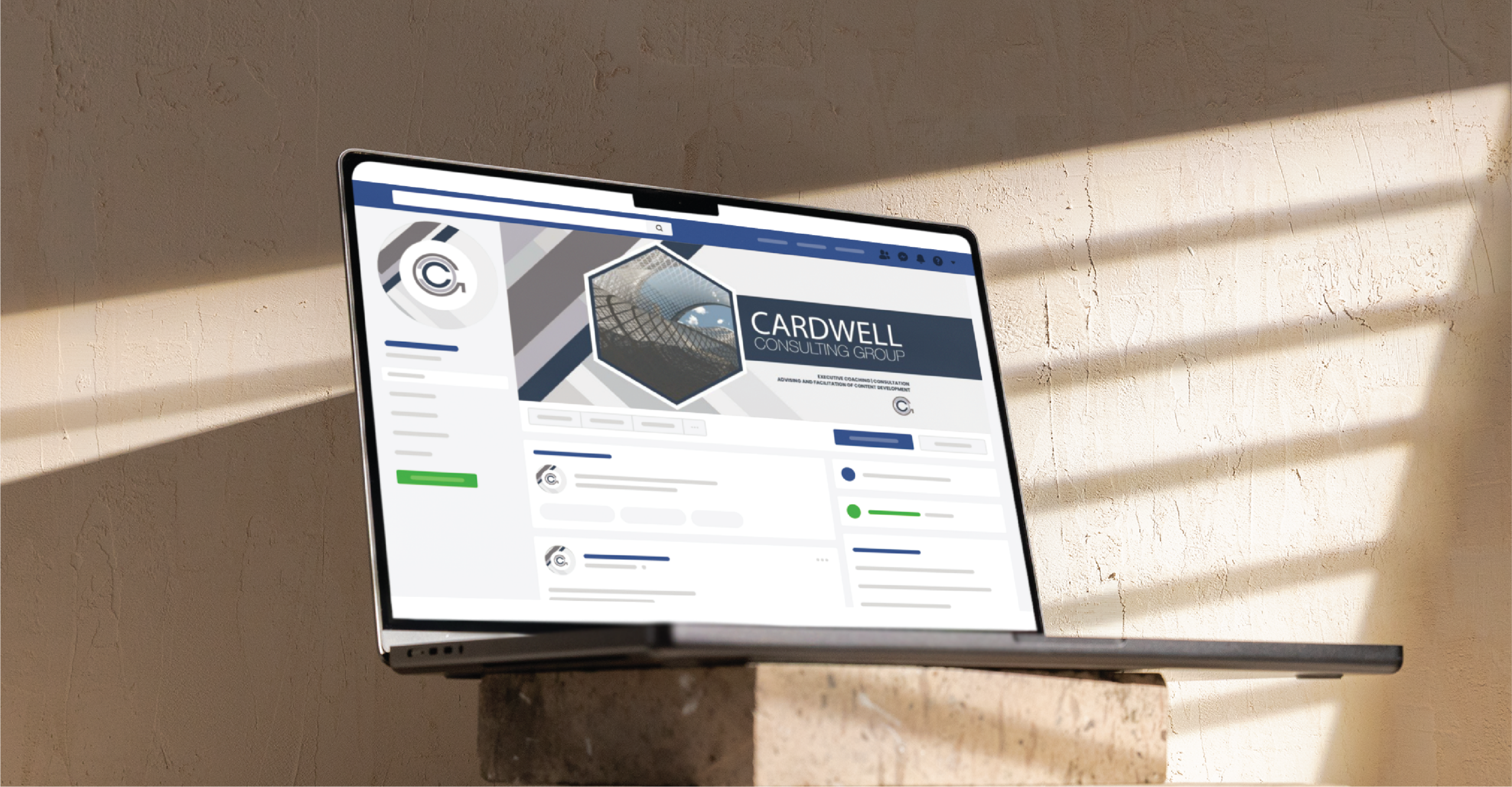 A laptop displaying the Facebook page of Cardwell Consulting Group, an HR Management firm in Minnesota, sits on a concrete block, illuminated by sunlight streaming through window blinds.