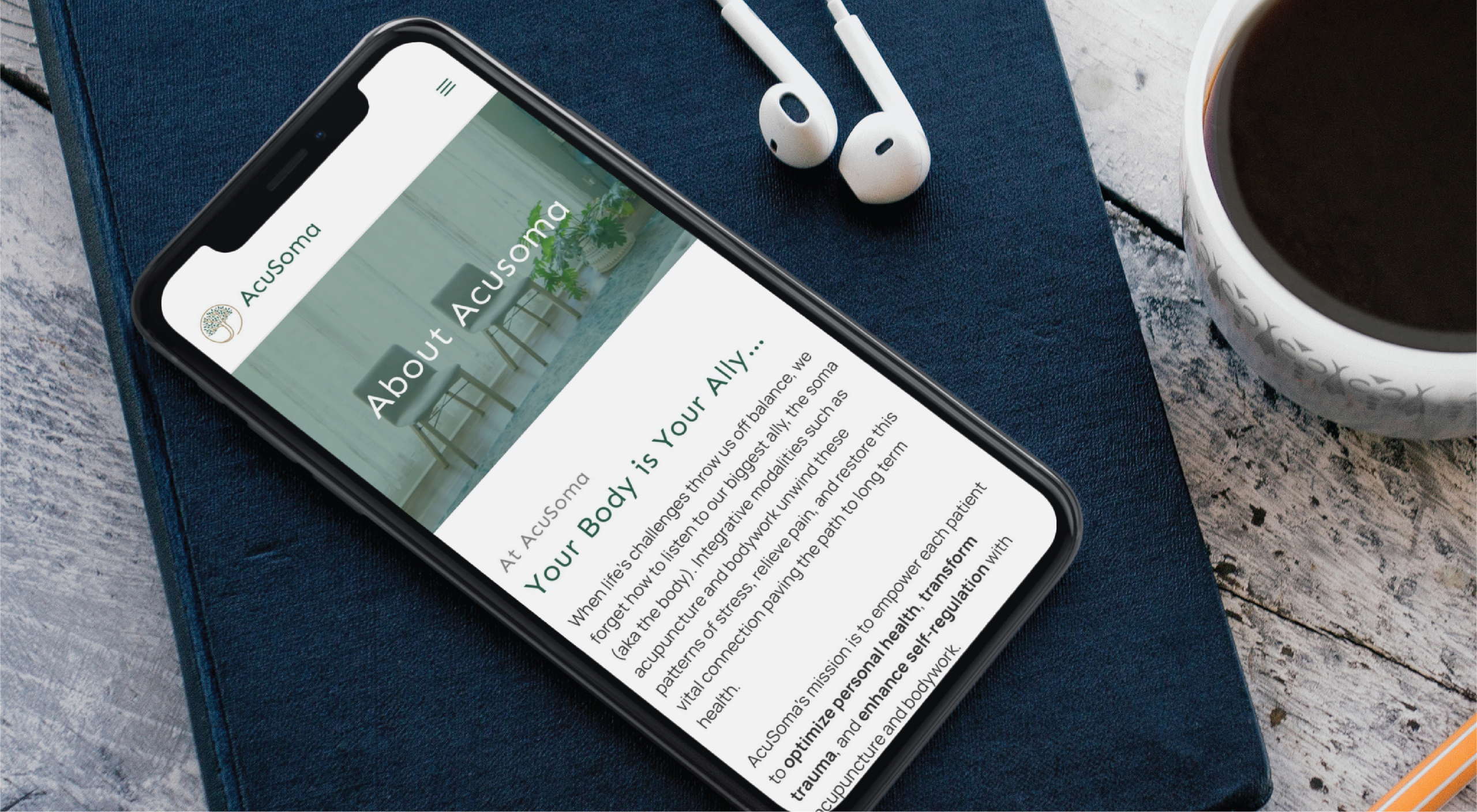 Smartphone on a blue notebook showing Acusoma's 'About' page, with earbuds and a coffee cup nearby.