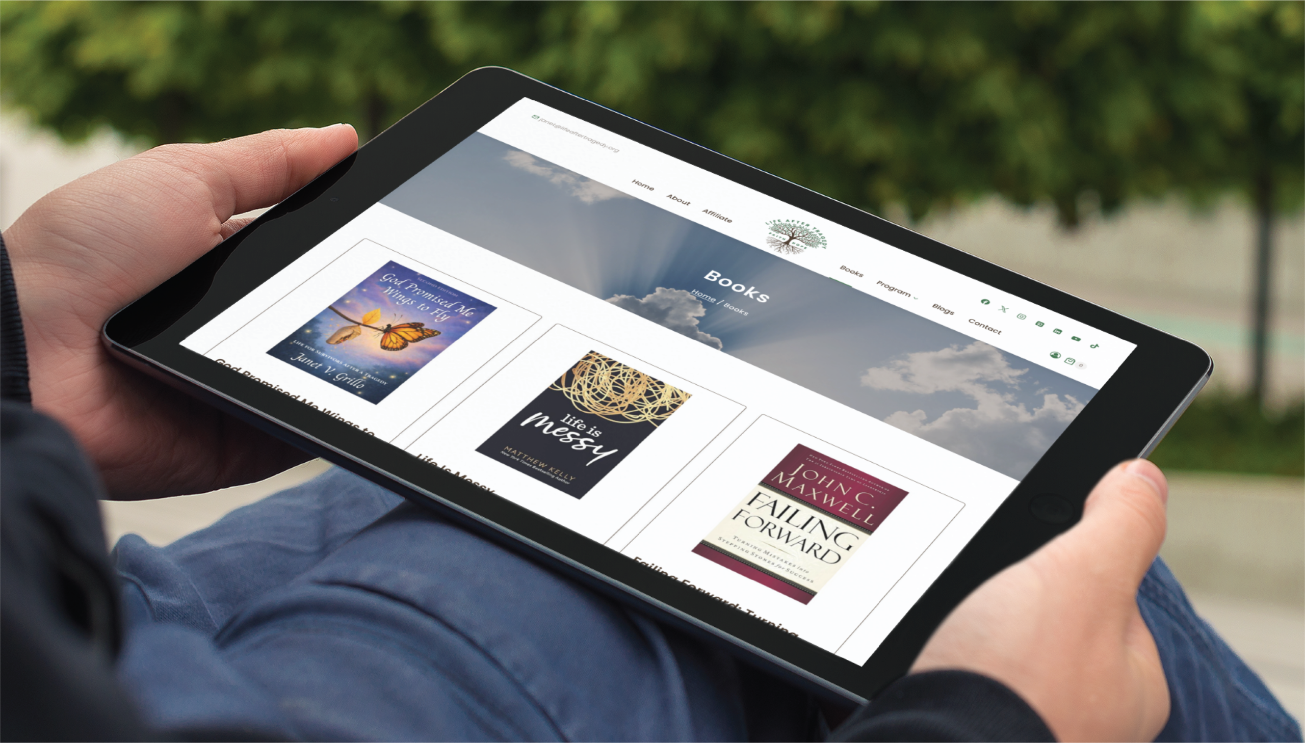 A person in Florida holds a tablet outdoors, browsing a website showcasing books like Life After the Storm, Battlefield of the Mind, and Failing Forward, with blurred trees in the background—a great example of modern website creation.