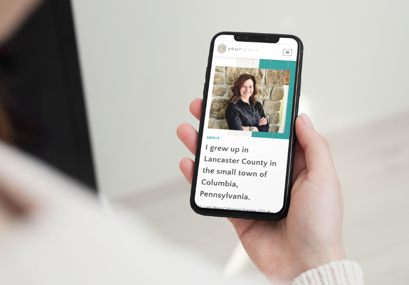 A person holding a smartphone displays a trustworthy website featuring a photo of a smiling woman and text about growing up in Columbia, Pennsylvania, in Lancaster County.