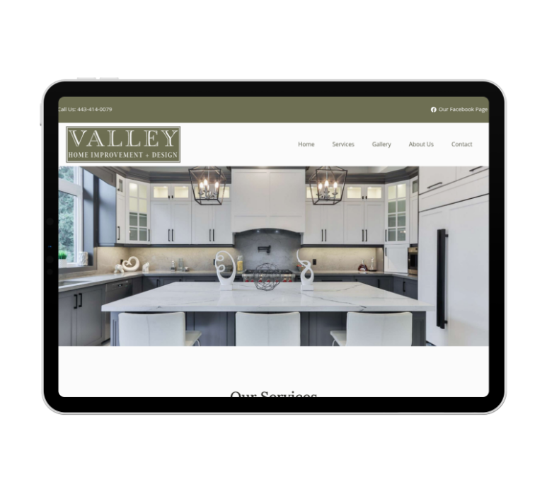 Tablet displaying the homepage of Valley Home Improvement + Design, showcasing their sleek website design with a modern kitchen scene—white cabinets, large island, pendant lights, and a clear navigation menu at the top for this leading construction company.