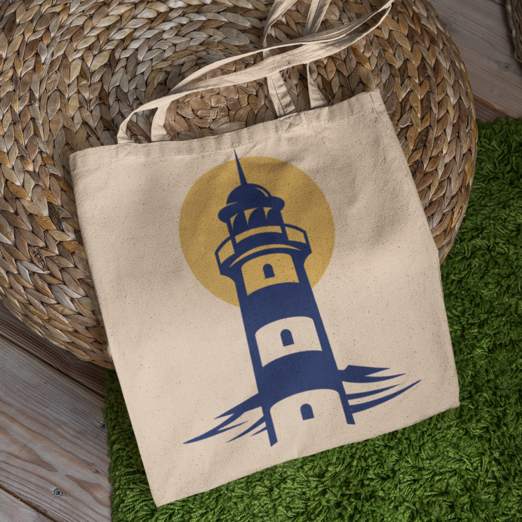A beige tote bag featuring a navy blue lighthouse and yellow sun design, inspired by thoughtful brand design, rests on a woven mat beside a green rug on a wooden floor.