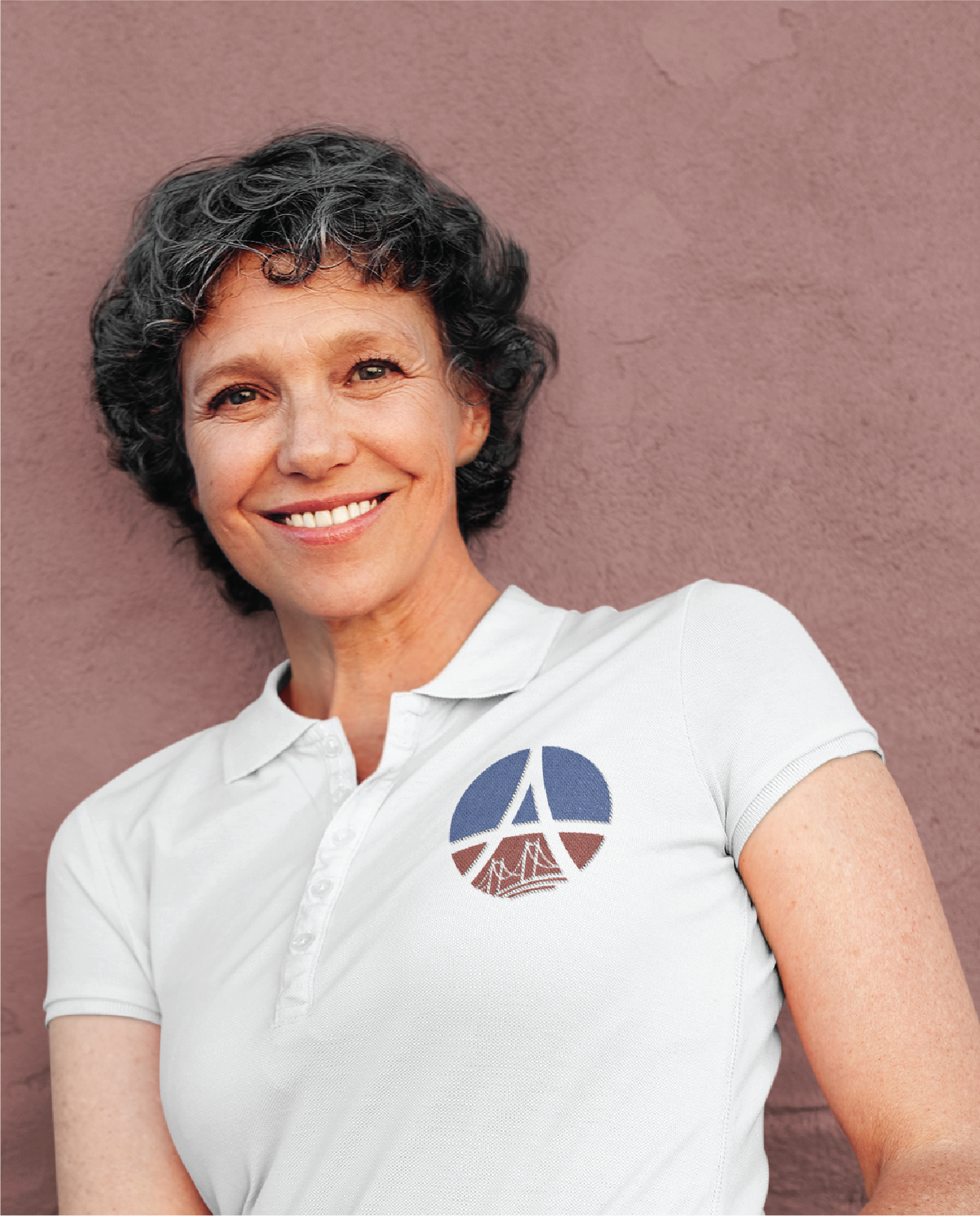 A smiling woman with short curly hair wearing a white polo shirt featuring a Nature Preserve logo design, standing in front of a textured pink wall.