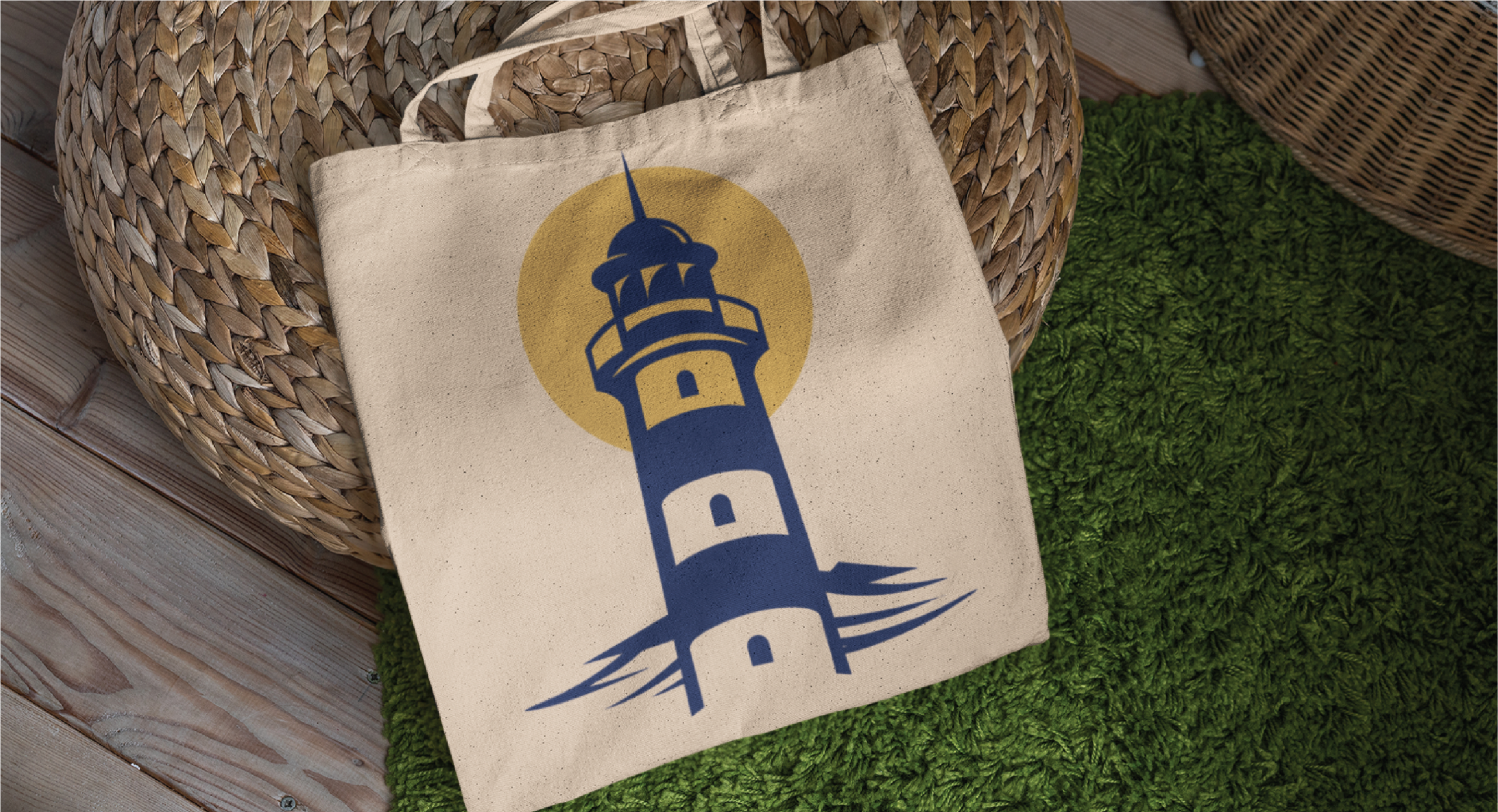 A beige tote bag with a blue and yellow lighthouse logo design rests on a wicker basket next to a green rug and wooden floor.