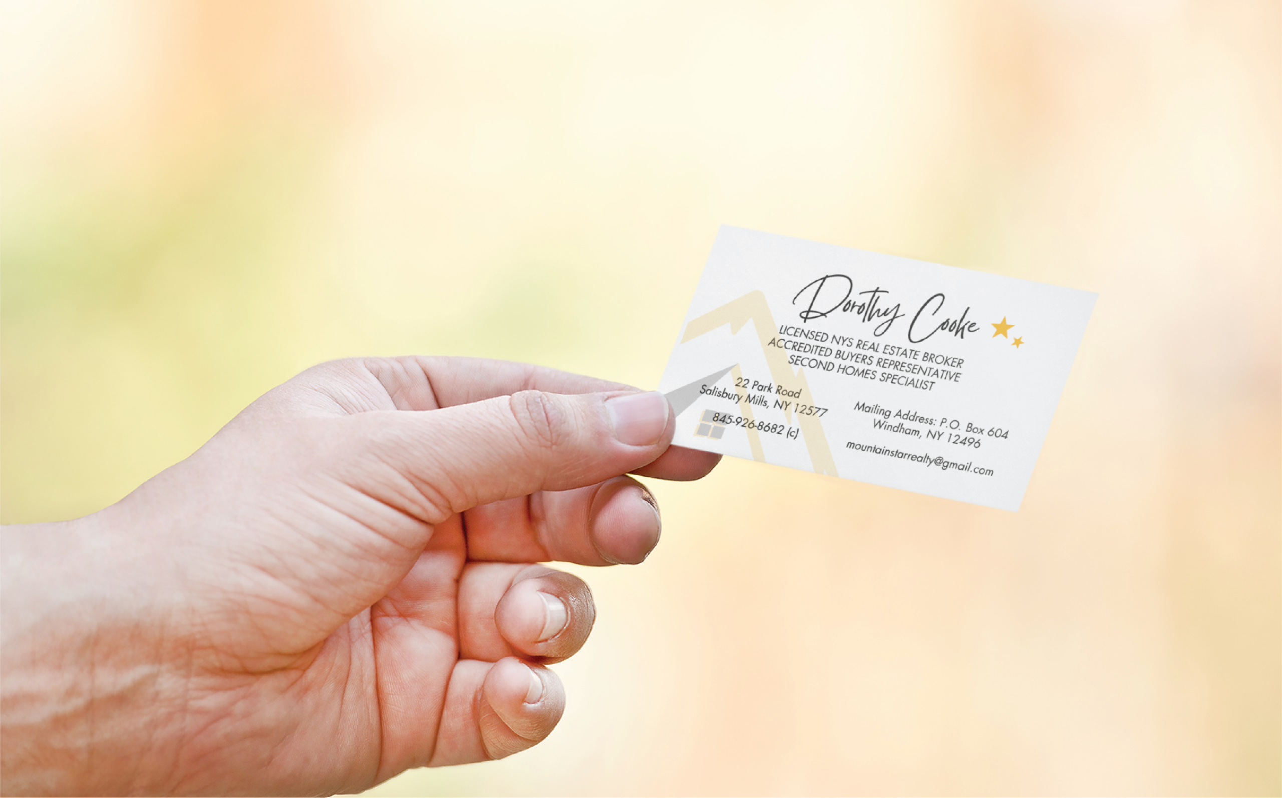 custom print design for realtors | Moonlit Media LLC A hand holding a business card for Mountain Star Realty, a licensed real estate broker and second homes specialist in New York, featuring contact details and sleek stationery design with minimal graphics.