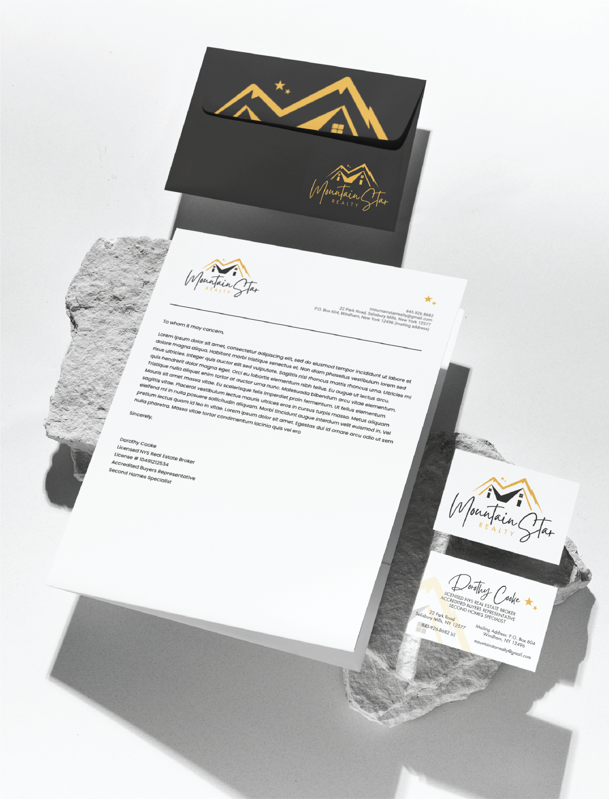custom stationery and print design | Moonlit Media LLC A branded stationery set for Mountain Star Realty in Michigan featuring a letterhead, business card, and envelope with a gold mountain logo, displayed on textured stone surfaces with clean, modern stationery design.
