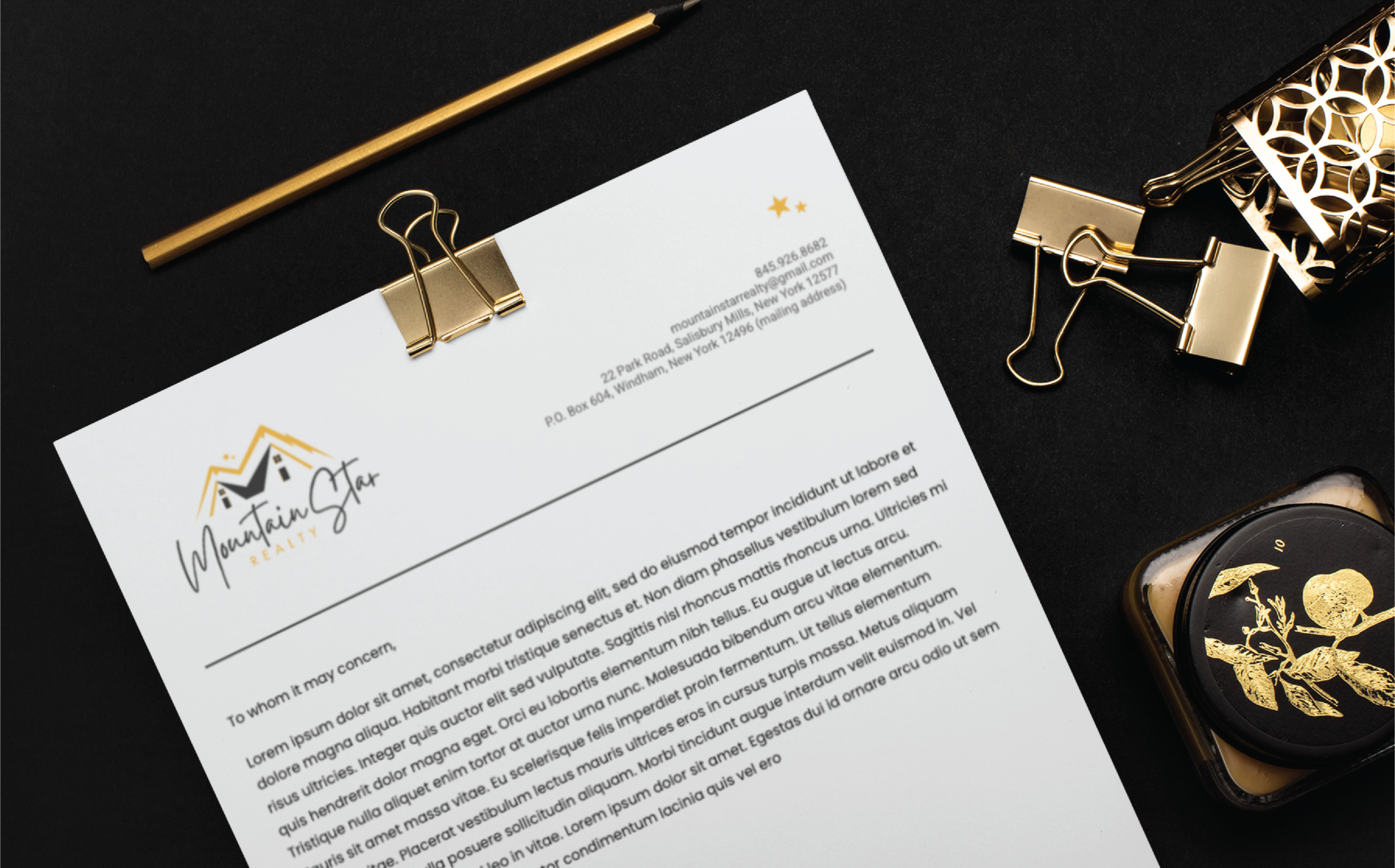 letterhead and print design for realty business | Moonlit Media LLC A letterhead with the Mountain Star logo, contact details, and placeholder text lies on a black surface with gold paper clips, a pencil, and a decorative ink bottle—exemplifying sophisticated stationery design for a Michigan general contractor.