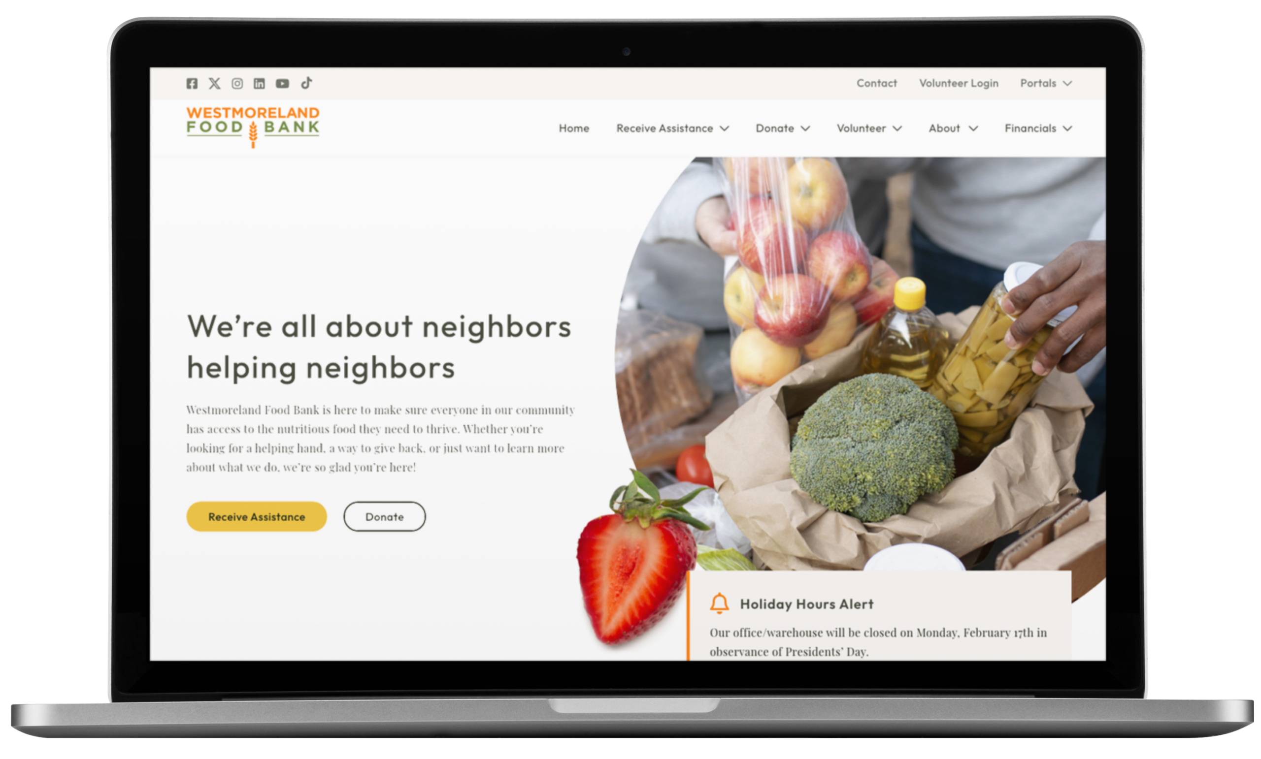 A laptop displays the Westmoreland Food Bank website, showcasing its thoughtful website design with text about helping neighbors, a photo of groceries including bread, apples, and pickles, plus buttons for assistance and donations.
