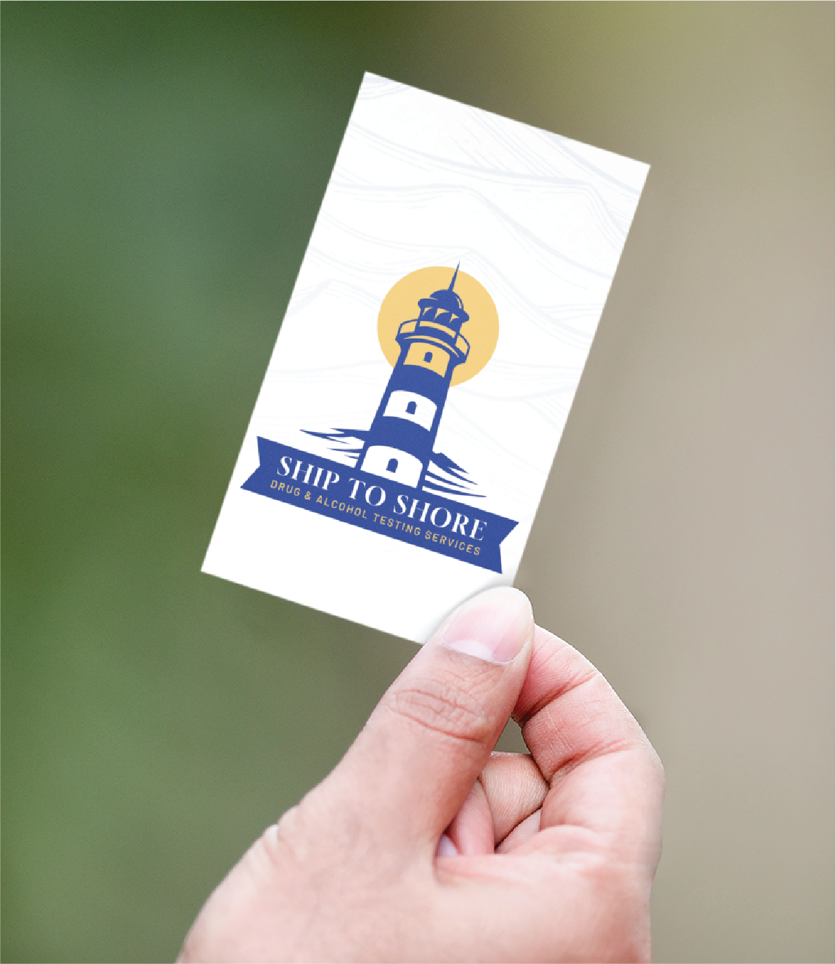 A hand holds a business card featuring a lighthouse logo with a yellow sun behind it. The card reads Ship to Shore Drug & Alcohol Testing Services, showcasing professional logo design against a blurred background.