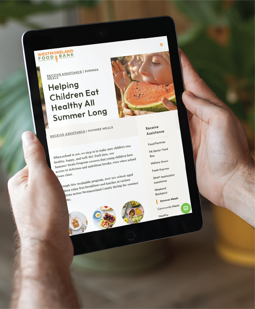 Person holding a tablet displaying the Westmoreland Food Bank website, showcasing its user-friendly website design with a headline about helping children eat healthy all summer, an image of a child eating watermelon, and a menu offering various assistance options.