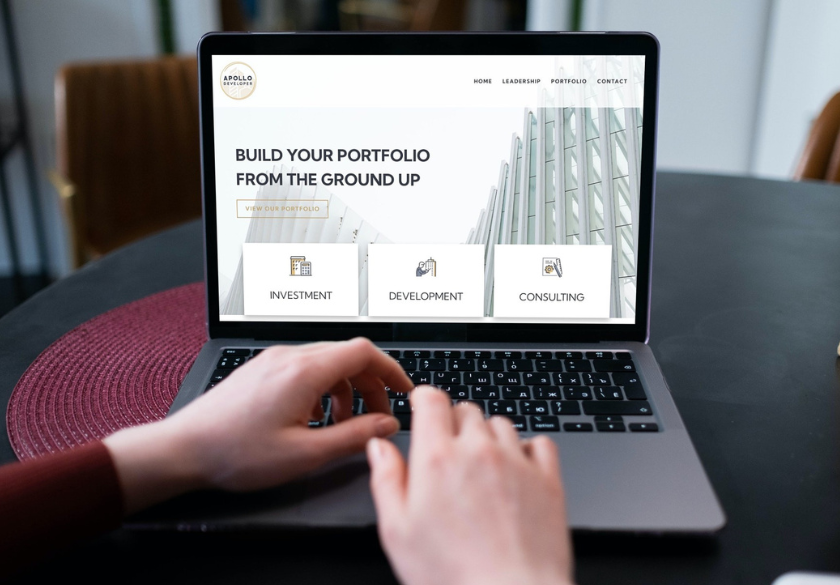 A person types on a laptop displaying a website with the headline Build Your Portfolio From the Ground Up and options for investment, development, and consulting—highlighting modern Small Business Website Design in the site’s background image.