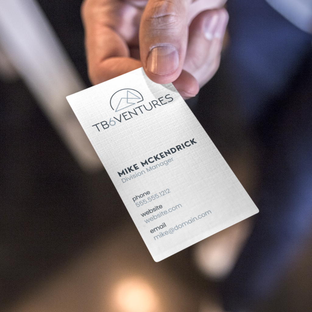 A person holds out a business card for TB6 Ventures in Michigan, featuring Business Card Design details for Mike McKendrick, Division Manager, with visible contact information including phone number, website, and email address.