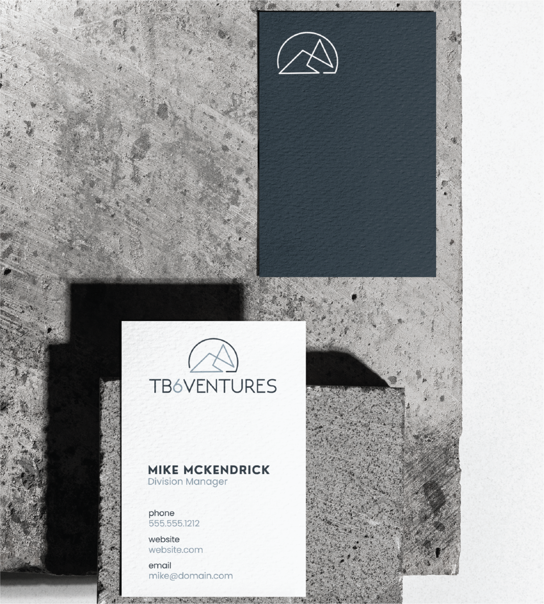 Two business cards for TB6VENTURES rest on textured concrete blocks, showcasing refined Business Card Design. One card is dark blue with a geometric logo; the other, white, displays Mike McKendrick's details and highlights Michigan excellence in Business Service.